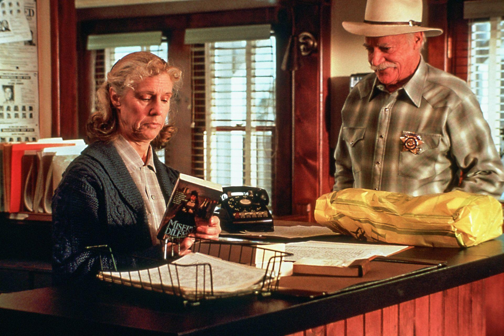 Eine Frau liest ein Buch, ein Mann in Sheriff-Uniform steht daneben.