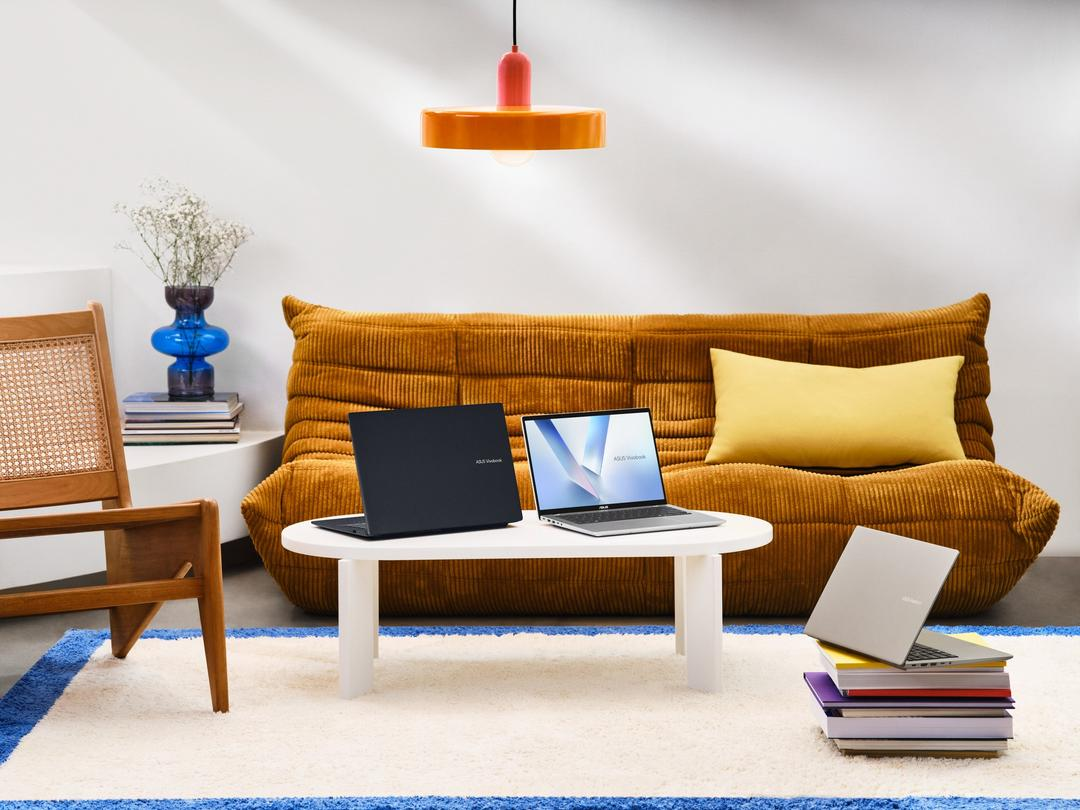 A room with a brown sofa, a white table with two laptops, and a chair. A lamp hangs above the table.