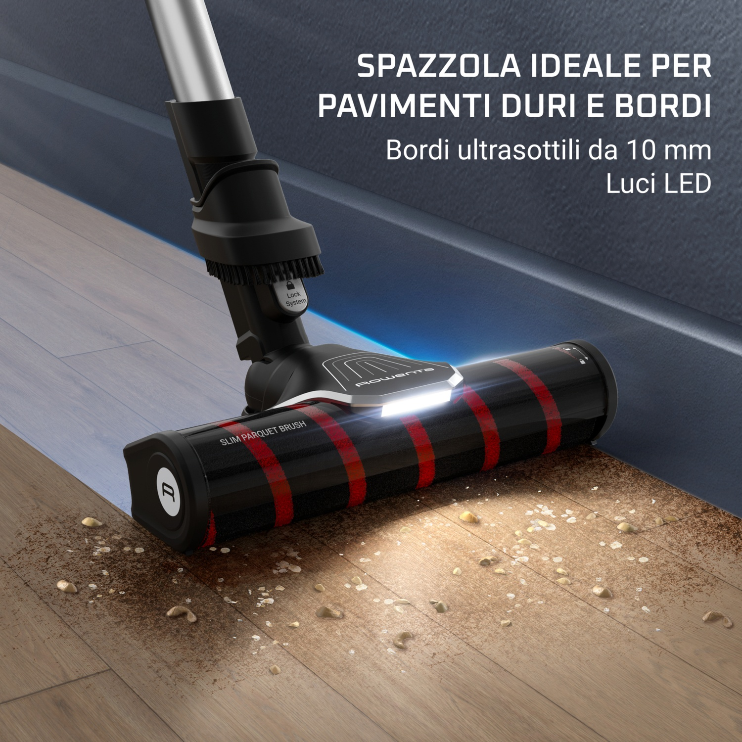 Testa dell'aspirapolvere su pavimento in legno. La testa è nera con strisce rosse e una luce. Ci sono briciole sul pavimento.