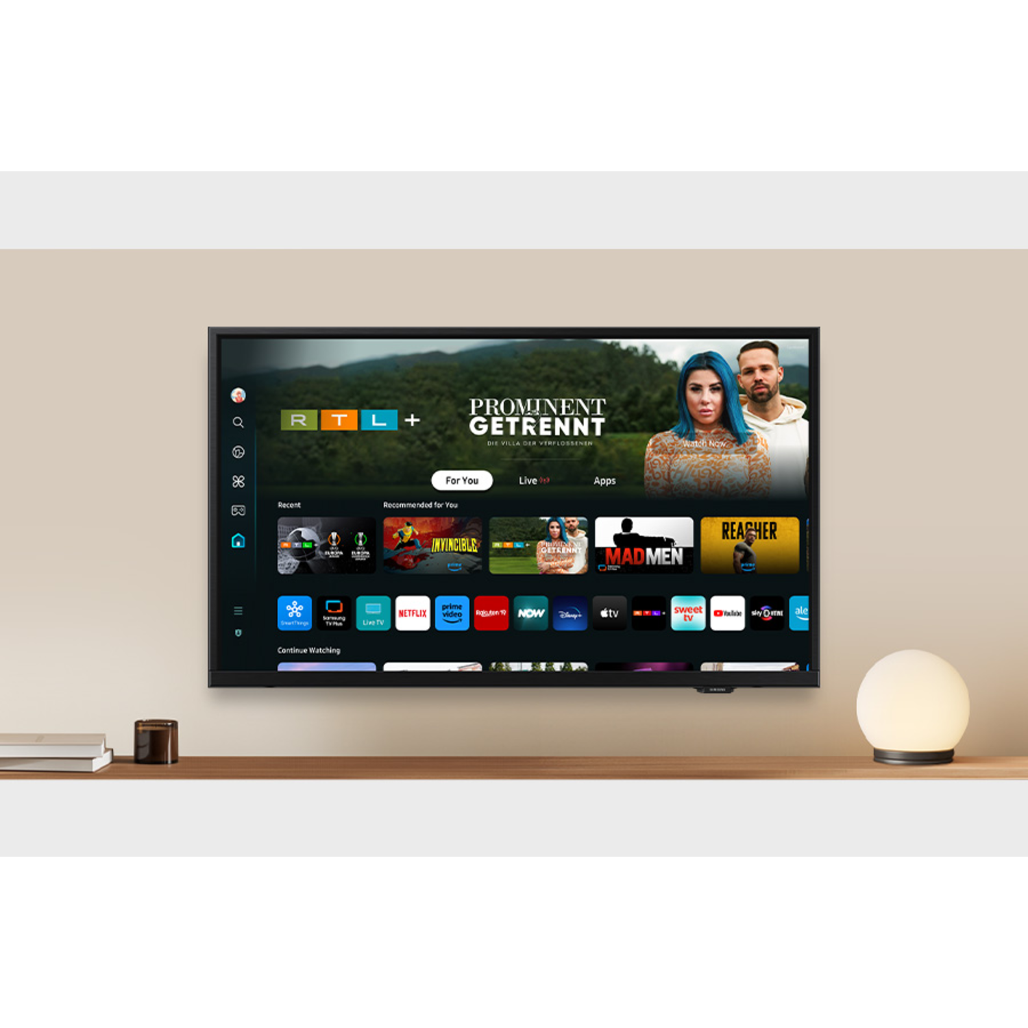 Television on a wooden shelf, showing a smart TV interface, with a lamp and books.