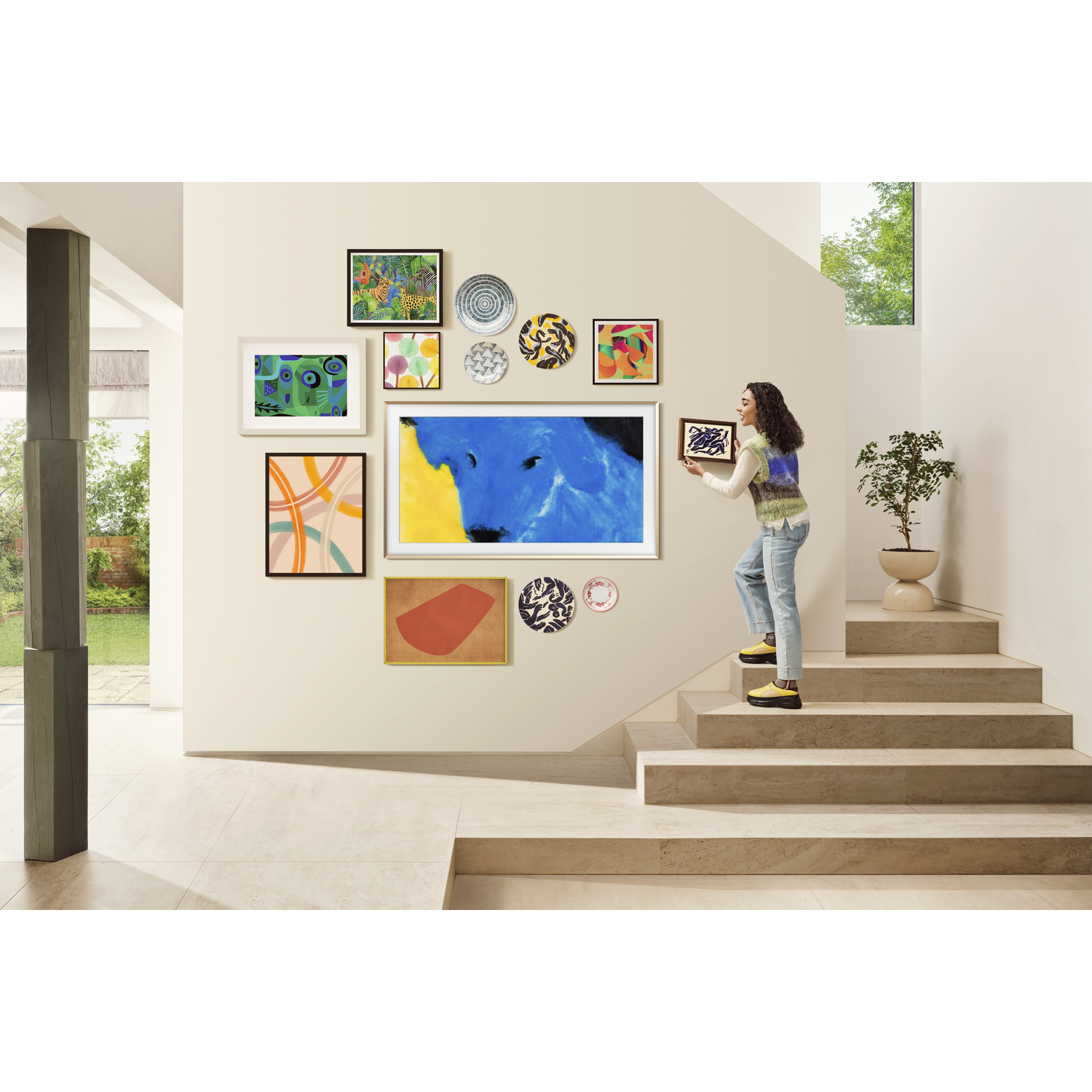 A woman hanging art on a wall. The wall has several pictures and art pieces.