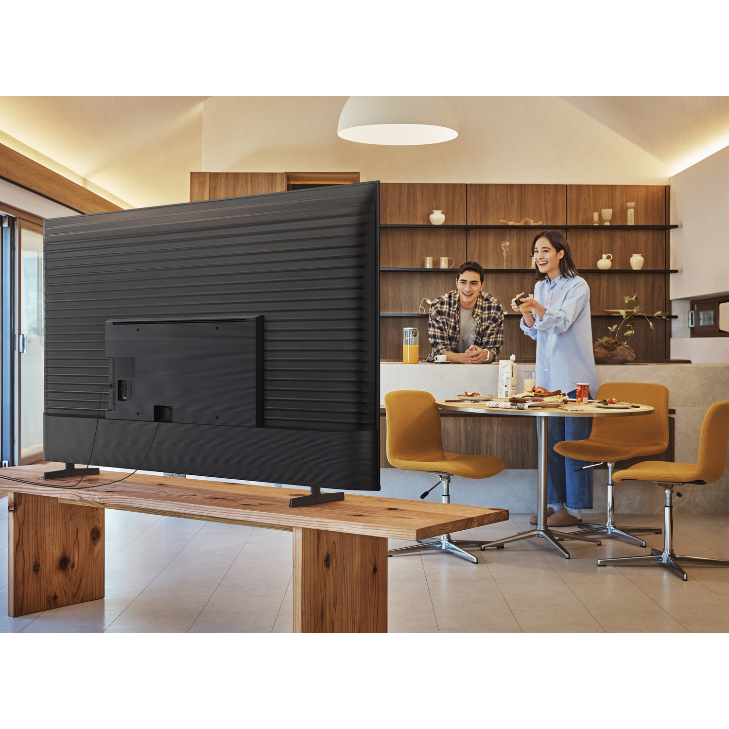 Een tv op een houten tafel, met een stel dat een spelletje speelt in een lichte woonkamer.
