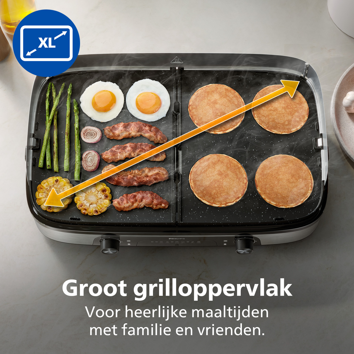 An electric grill with eggs, pancakes, bacon, asparagus, corn, and onions. XL size label is in the top left corner.