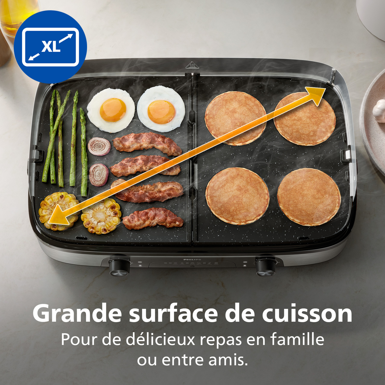 Un grill électrique avec œufs, crêpes, bacon, asperges et maïs. Icône XL et texte 'Grande surface de cuisson'.
