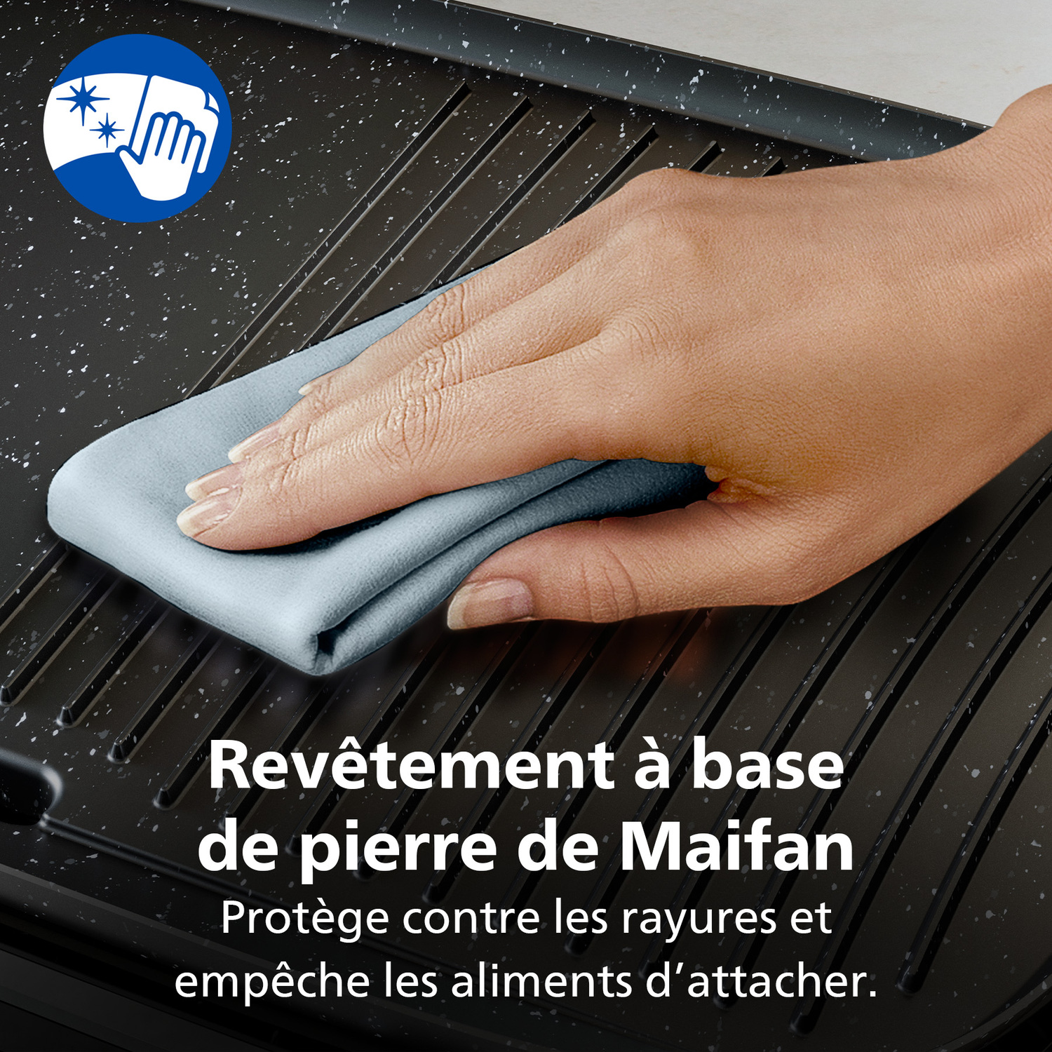 Une main essuie un chiffon gris sur un grill noir. Le grill a des mouchetures blanches. Le texte indique qu'il est revêtu de pierre de Maifan.