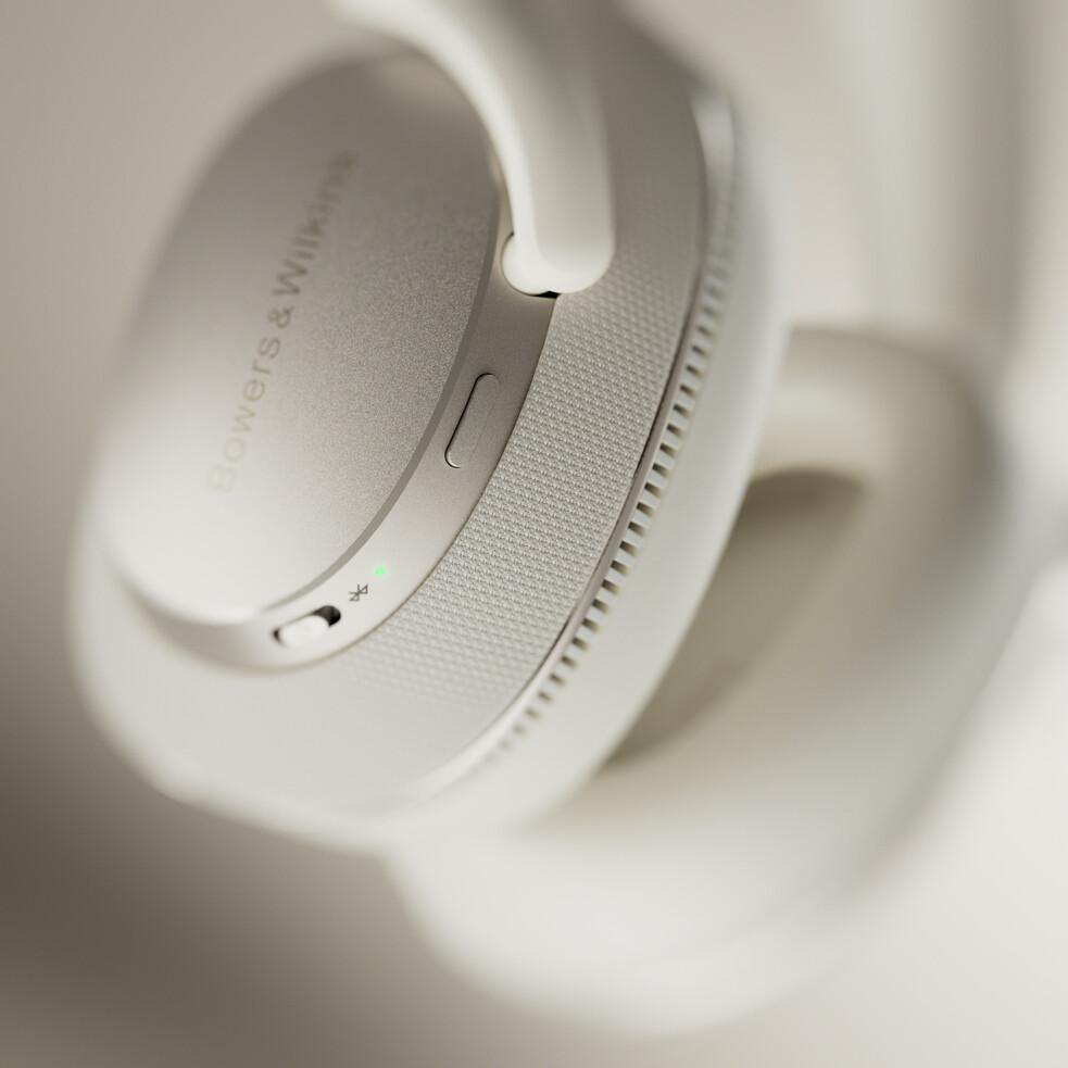 Nahaufnahme eines weißen Bowers & Wilkins Kopfhörers. Der Lautstärketaster und eine Statusleuchte sind sichtbar.