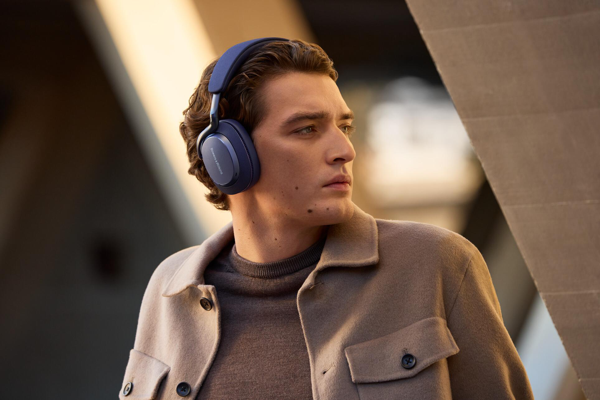 Ein Mann mit blauen Bowers & Wilkins Kopfhörern, vor unscharfem Hintergrund.