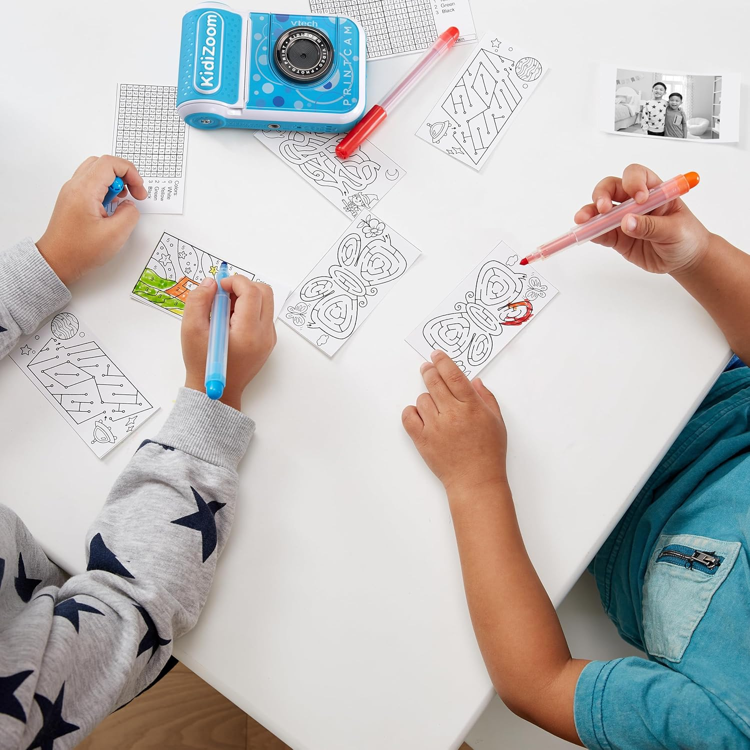Zwei Kinder malen Labyrinthe und Bilder, eine Spielzeugkamera in der Nähe.