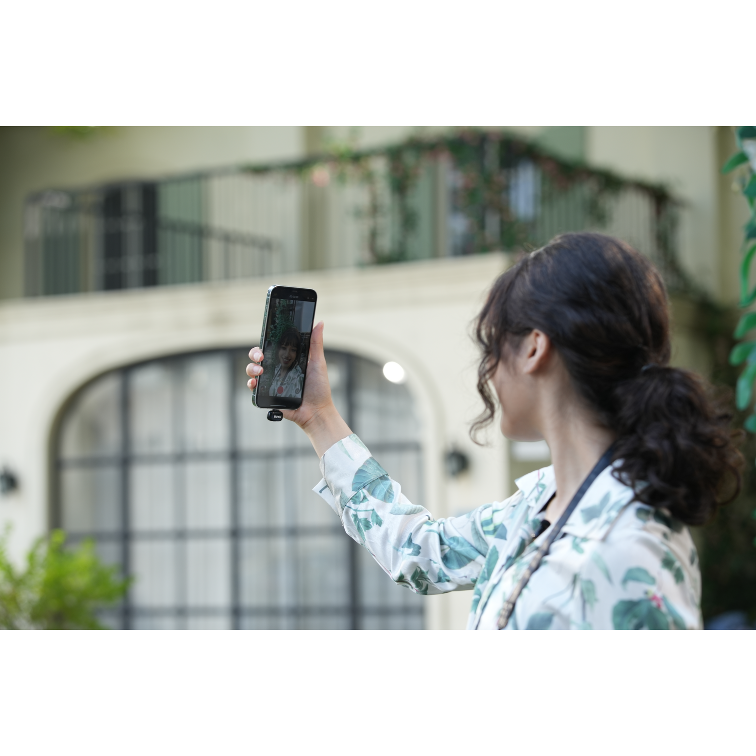Vrouw die een selfie maakt met een telefoon voor een gebouw met een bloemenjasje.