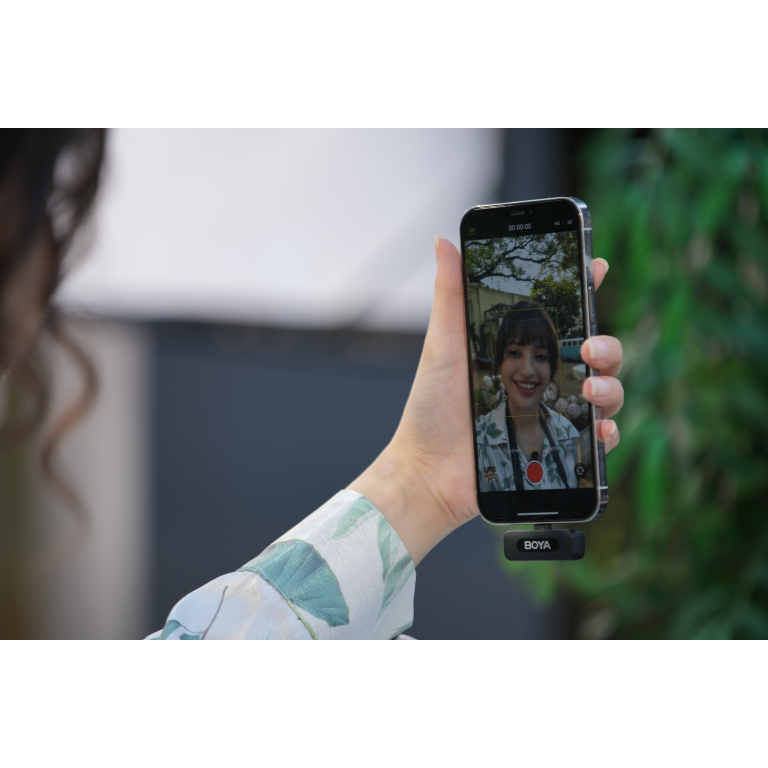 Een persoon die een smartphone vasthoudt, met een selfie en een Boya microfoon.