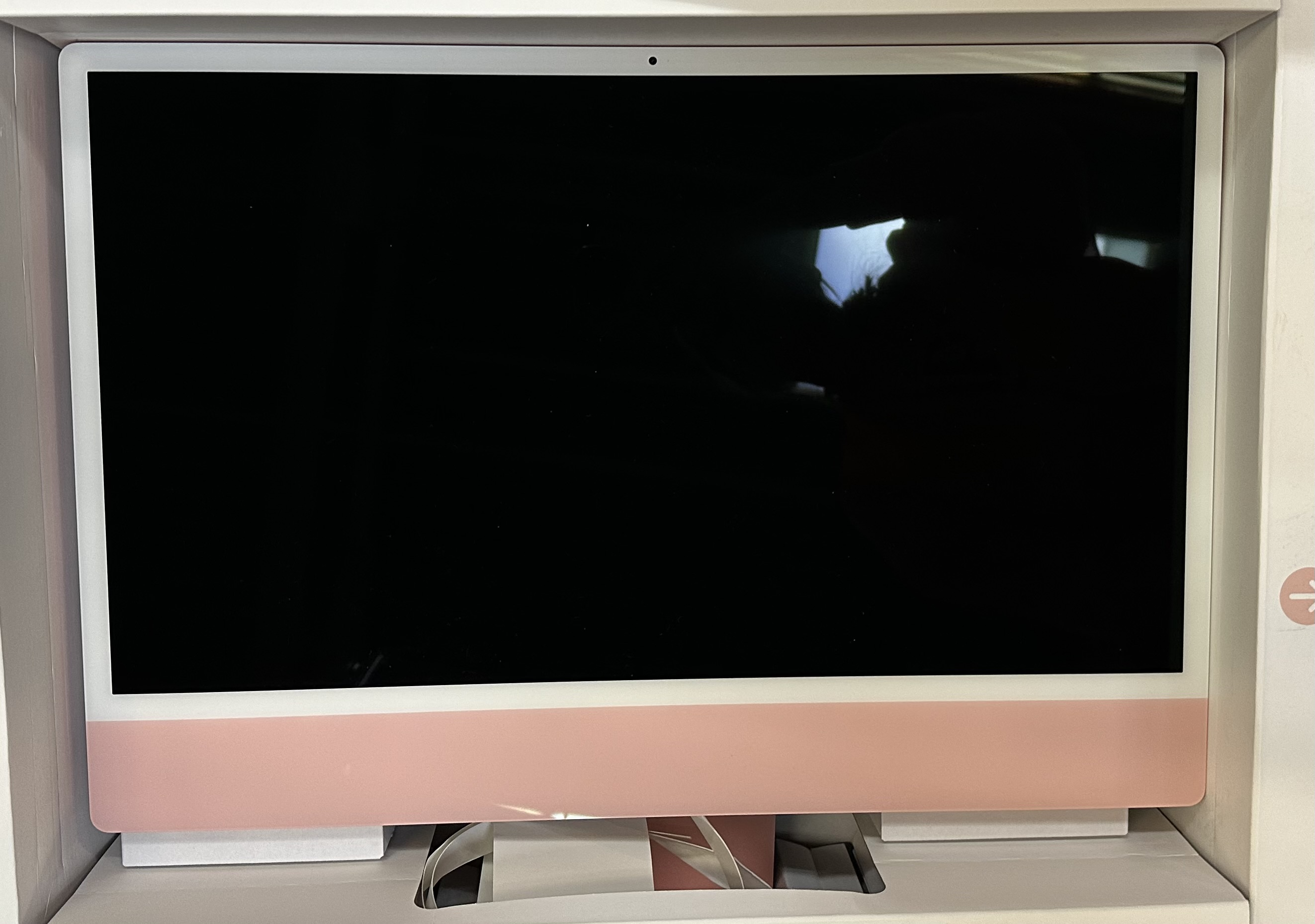 Różowy i biały komputer iMac wyświetlany w białym pudełku. Ekran jest czarny. Światło odbija się na ekranie.