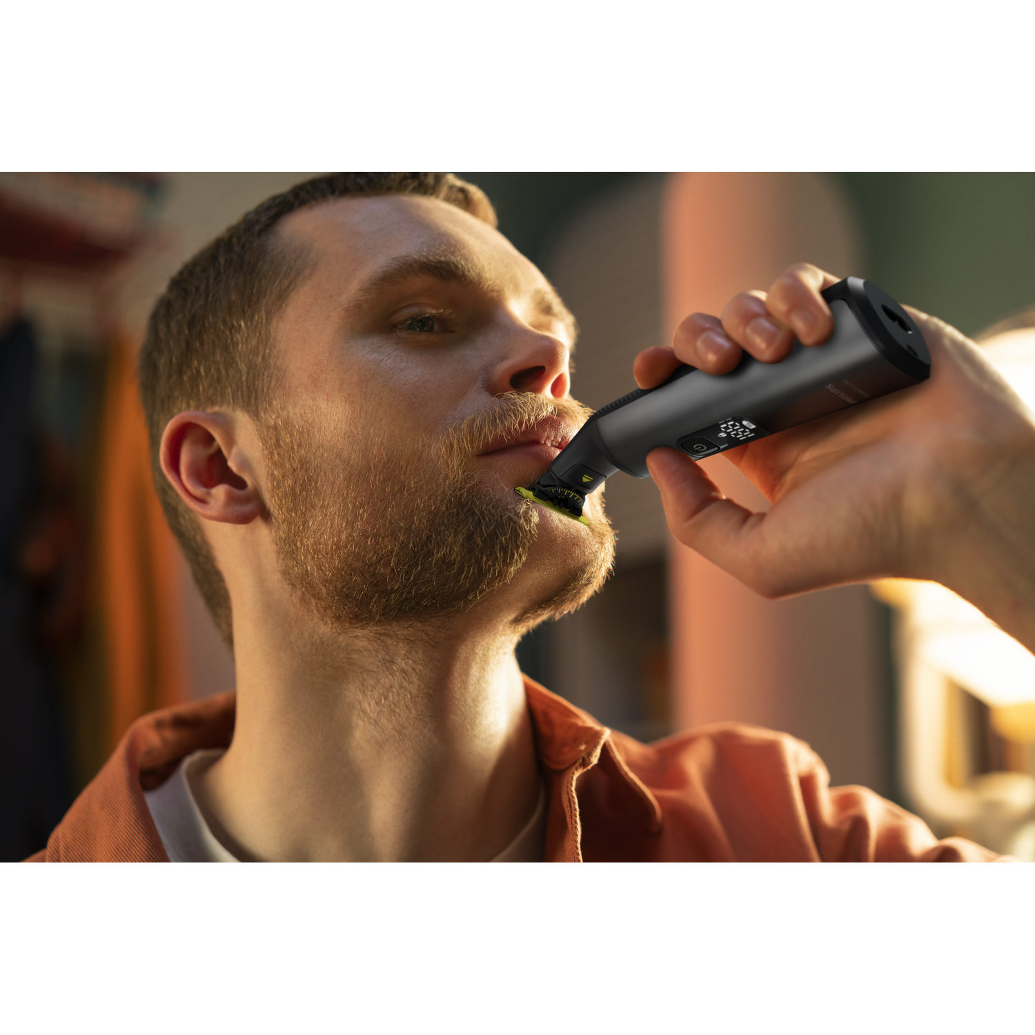 Man trimming his beard with a black trimmer. Focus on the trimmer and beard.