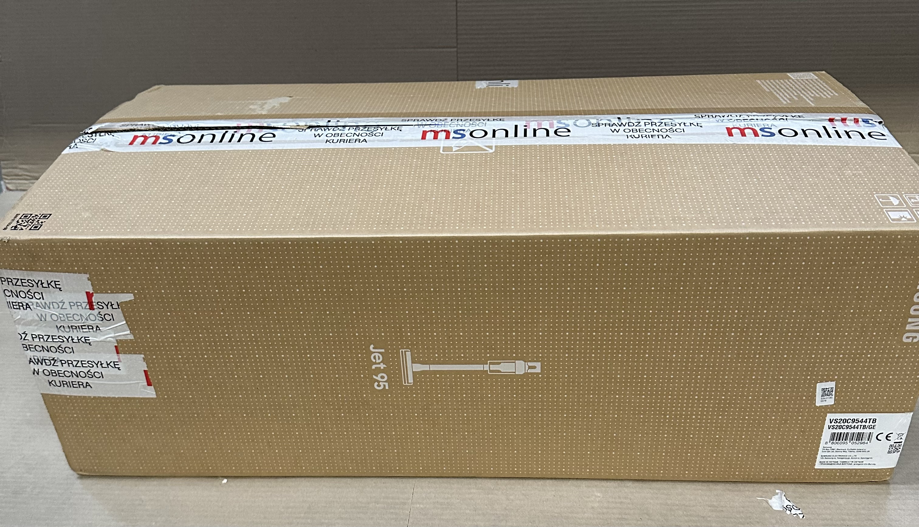 Duże kartonowe pudełko, z napisem 'msonline' i 'Jet 95', zaklejone taśmą, na powierzchni.