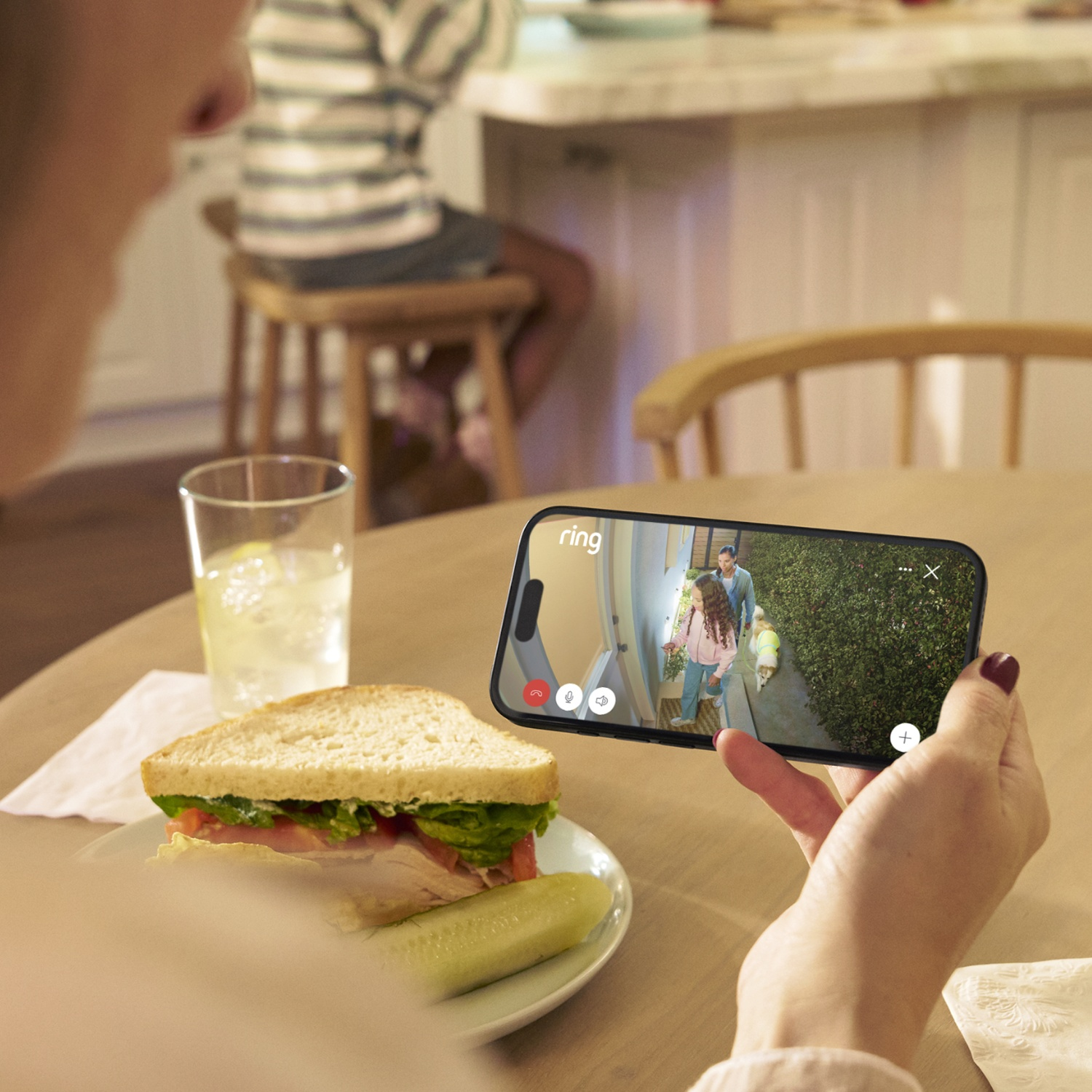 Donna che tiene un telefono che mostra una videochiamata con persone all'aperto. Panino e bevanda.