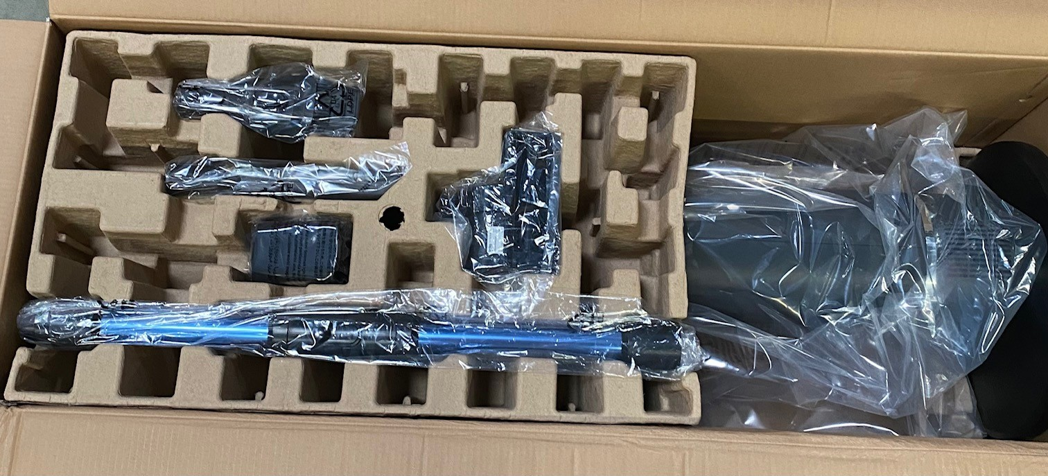 Wewnątrz pudełka od odkurzacza elementy są w plastiku, a niebieska rura jest widoczna.