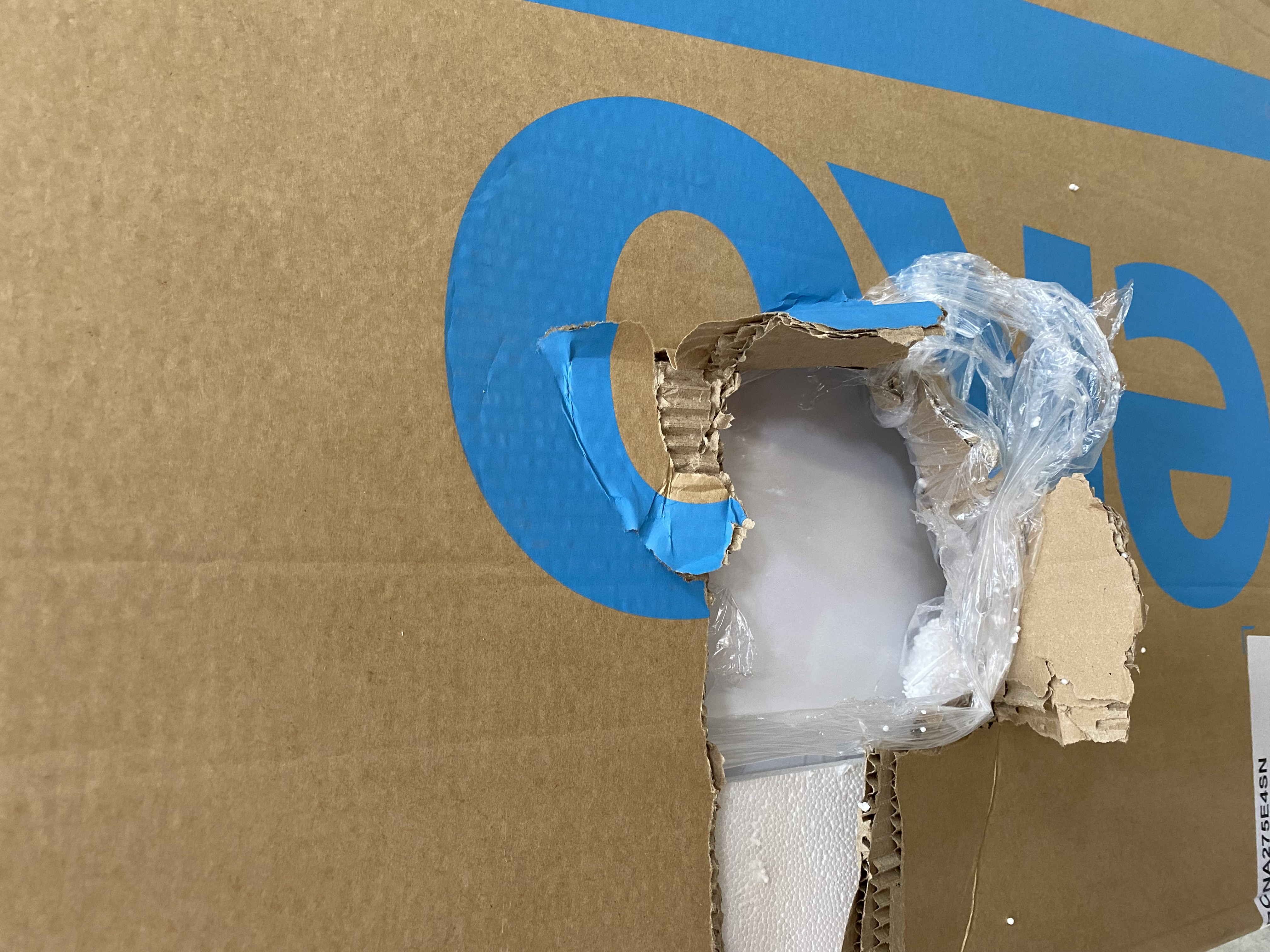 Uszkodzone pudełko kartonowe z taśmą i dziurą z widocznym plastikiem.