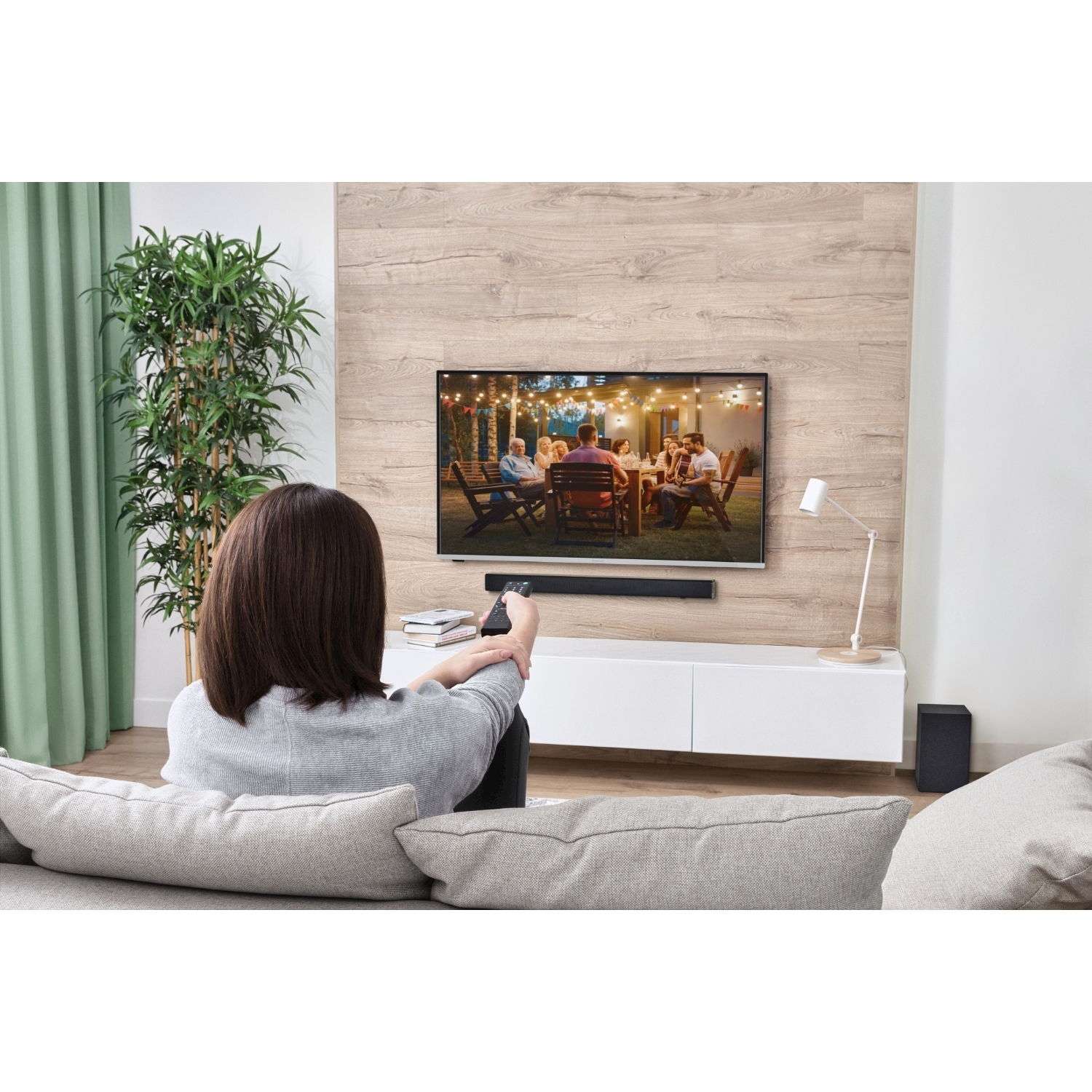 Una donna seduta, guarda la TV su una parete in legno, con soundbar e subwoofer.