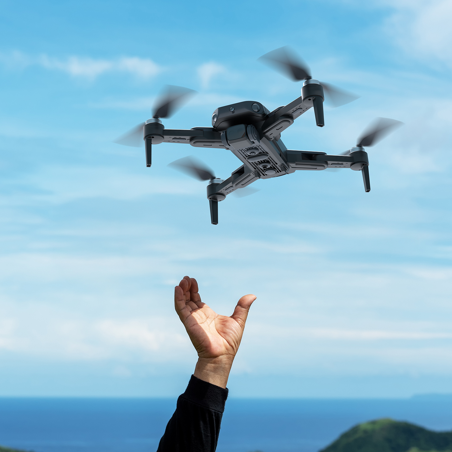 Bir drone, bulutlar ve okyanusla mavi bir gökyüzüne karşı uzatılmış bir elin üzerinde uçuyor.
