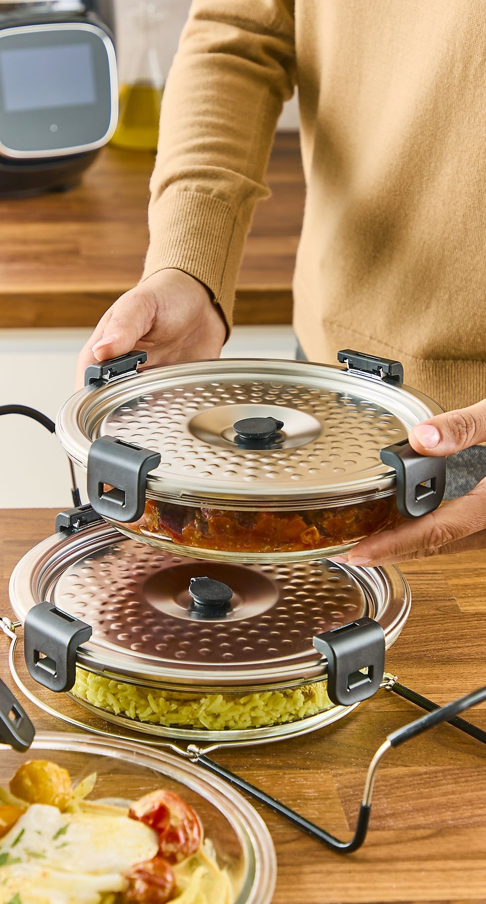 Osoba trzyma dwa szklane pojemniki z jedzeniem na drewnianej powierzchni.