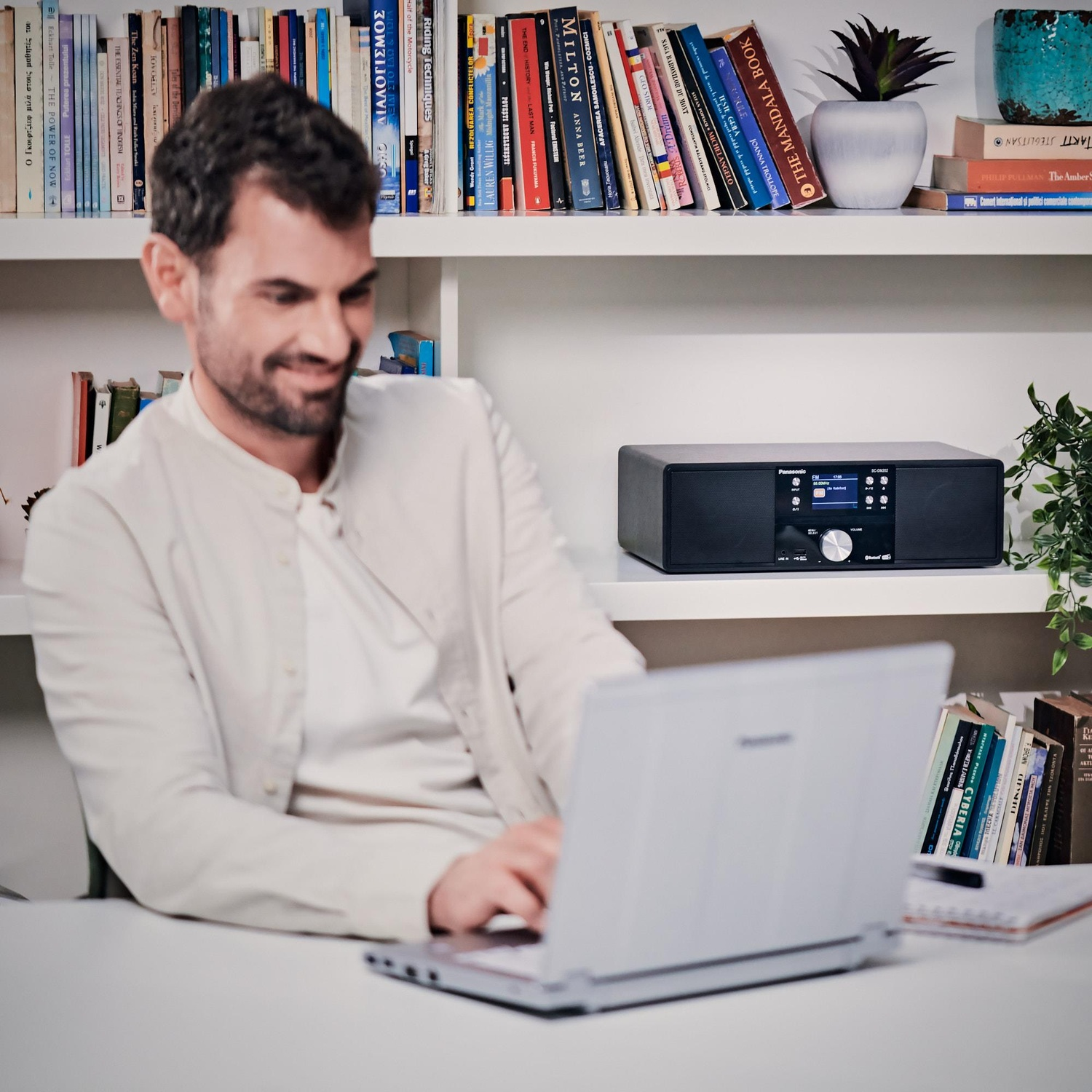 Uomo che usa un laptop, un impianto audio nero e libri sullo sfondo.