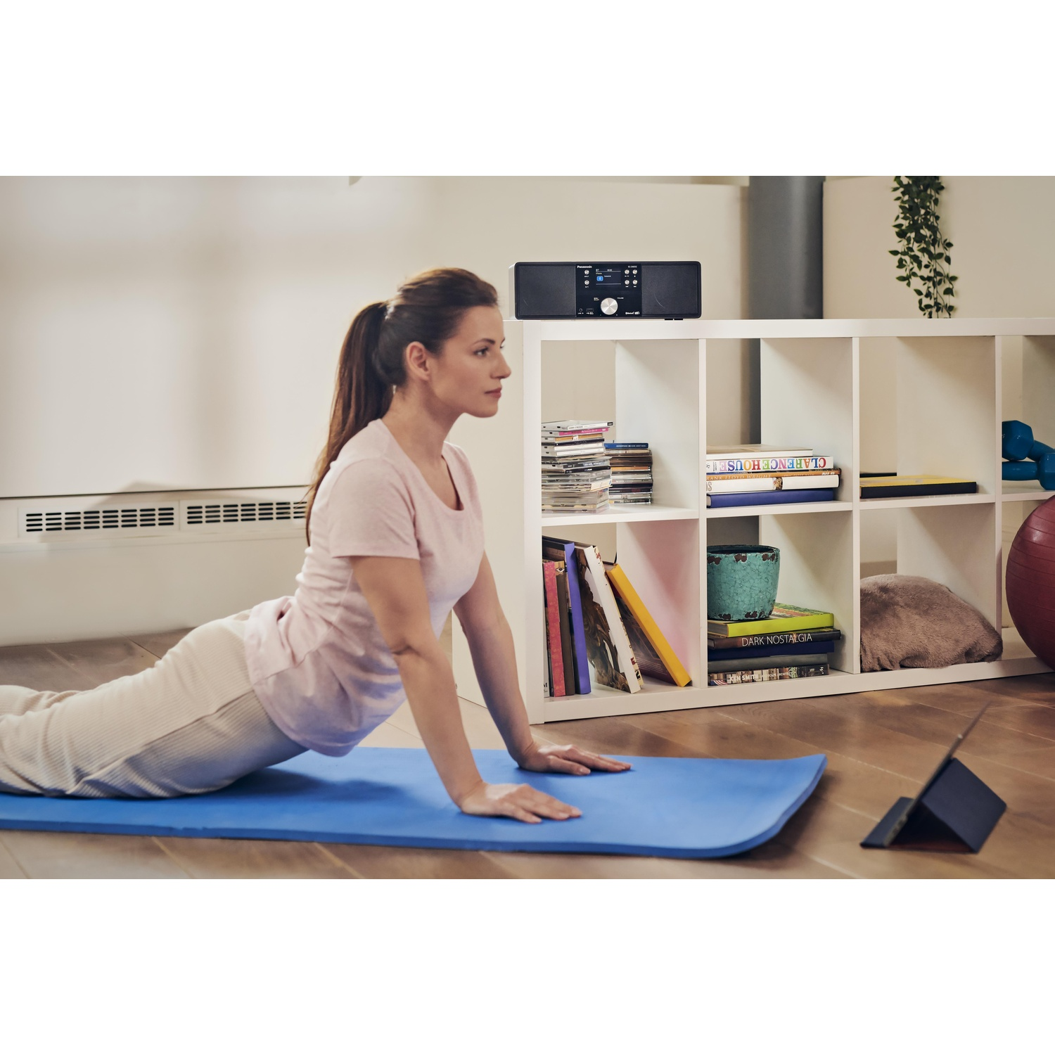 Donna che fa yoga su un tappetino blu, un impianto stereo e una libreria sullo sfondo.