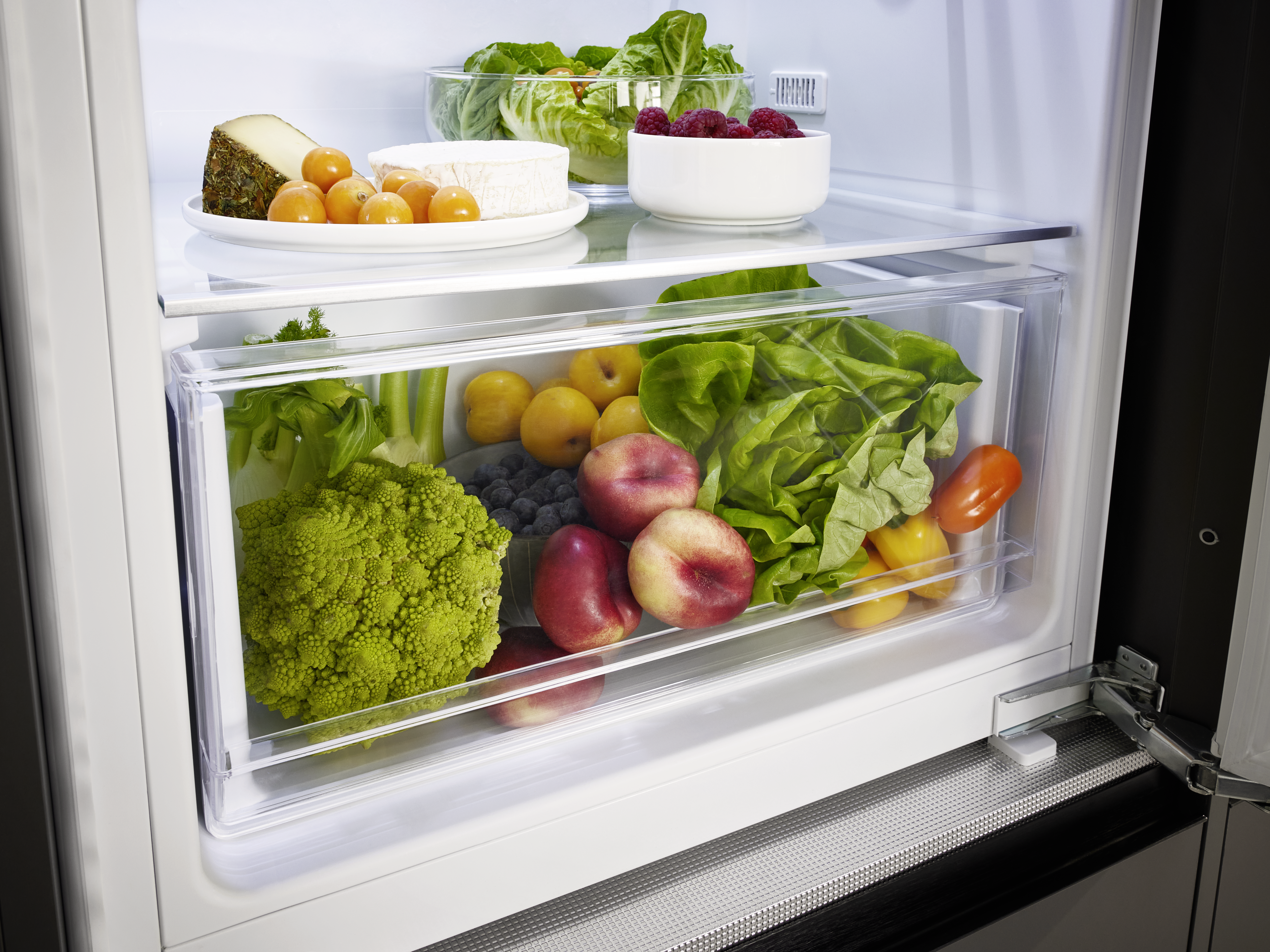 Kühlschrankinnenraum mit frischen Produkten. Obst, Gemüse und Käse in transparenten Behältern.