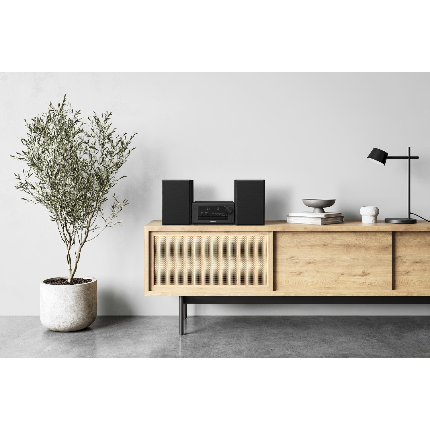 Un impianto stereo su un mobile in legno, con una pianta a sinistra. Una lampada nera a destra.