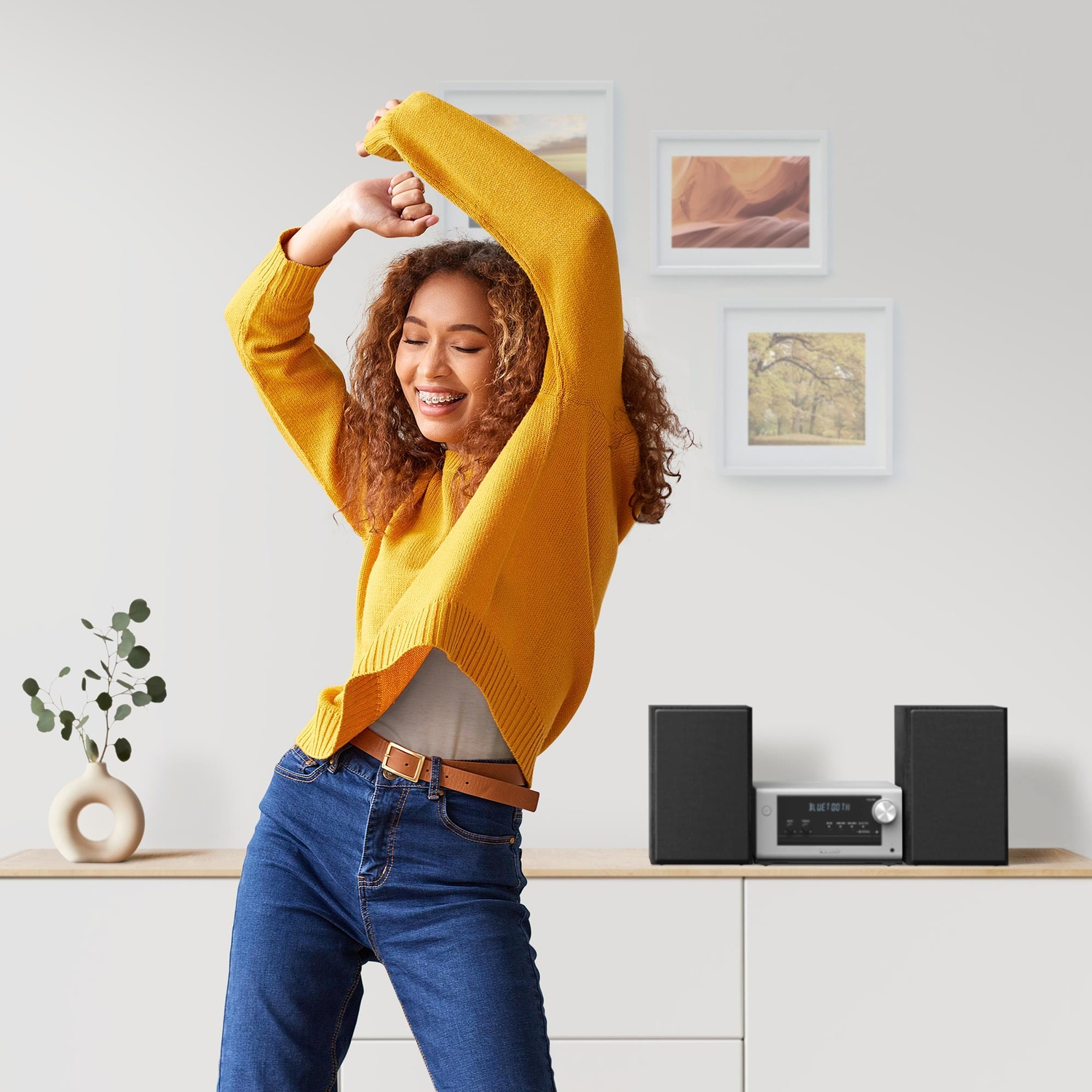 Una donna balla con un maglione giallo, impianto musicale e due altoparlanti su un bancone.