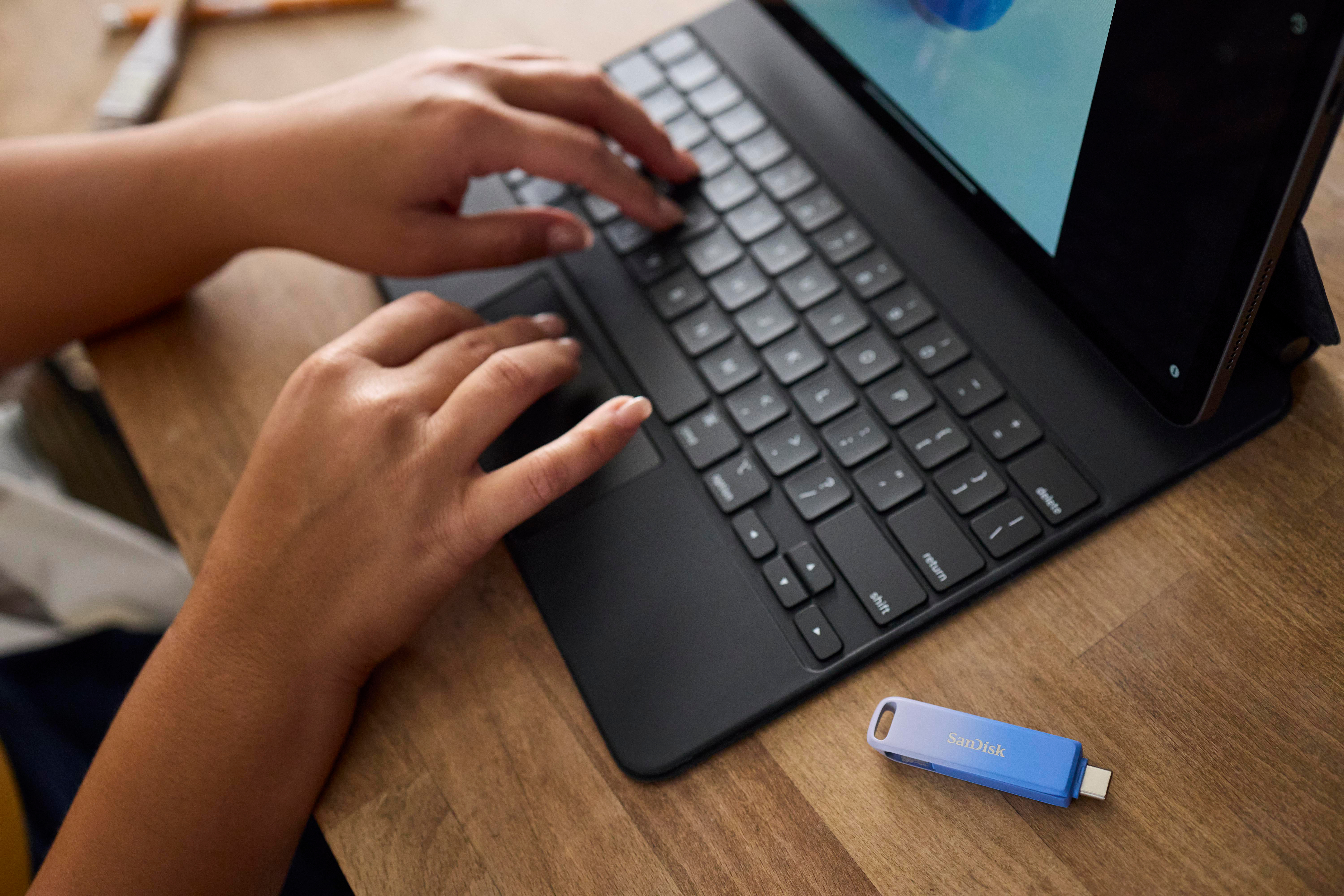 Hände tippen auf schwarzer Tastatur, verbunden mit Tablet, mit blauem USB-Laufwerk.