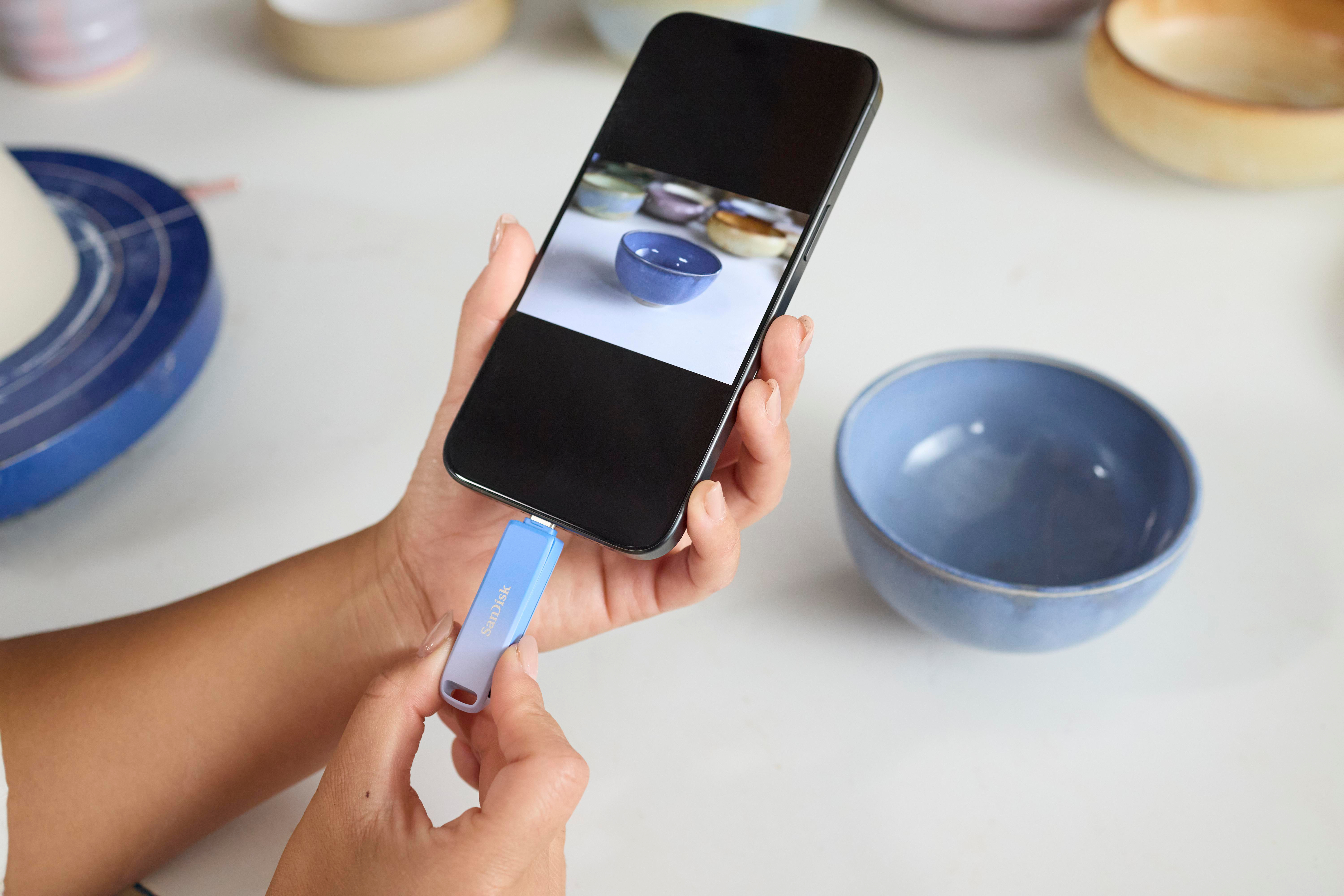 Eine Person hält ein Smartphone, das mit einem USB-Stick verbunden ist, mit Keramikschalen in der Nähe.
