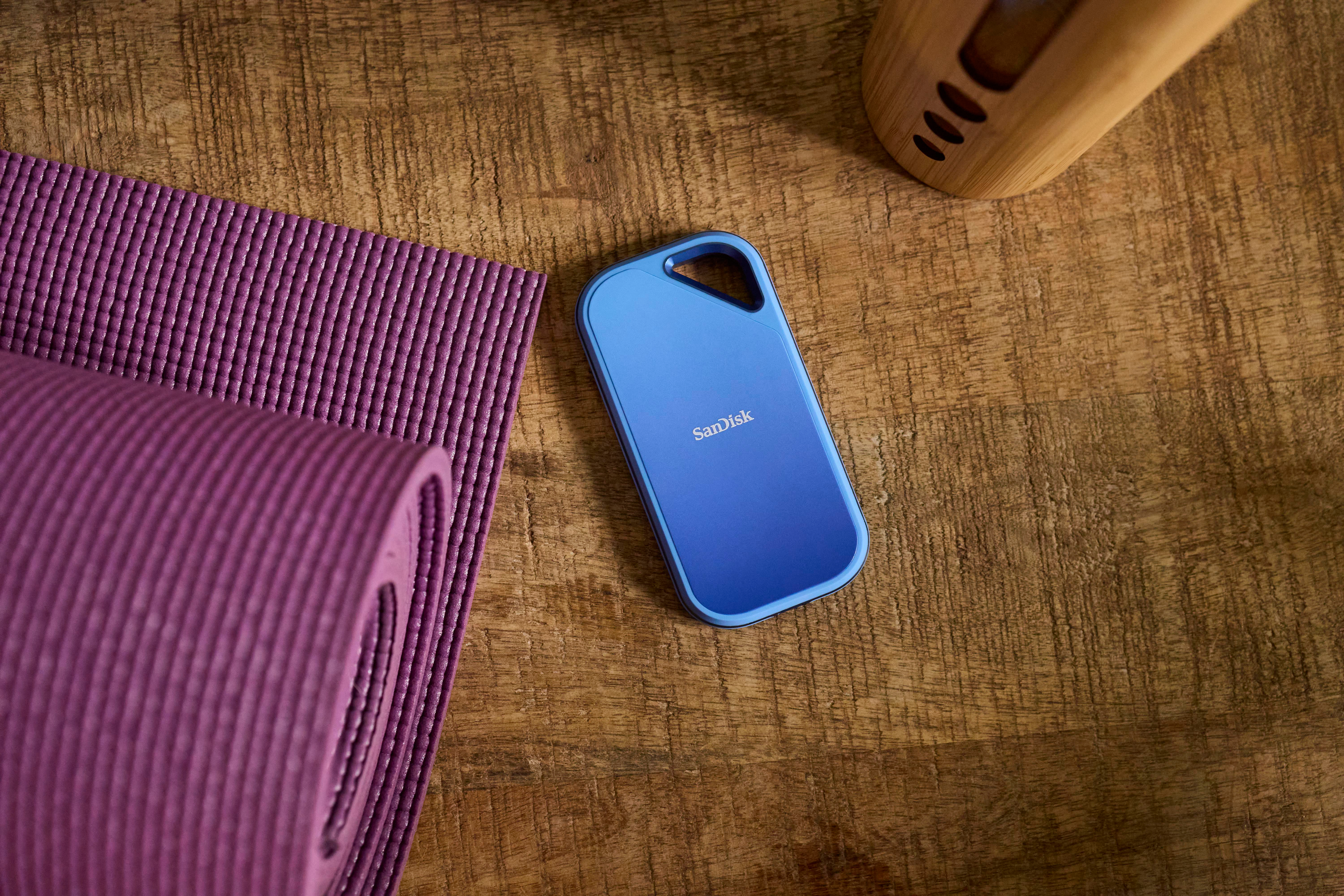 Blaue tragbare Festplatte auf Holztisch neben lilafarbener Yogamatte und Holzartikel.