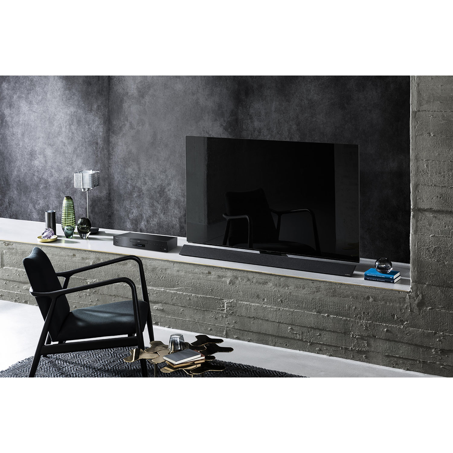 Soggiorno con TV su mensola in cemento, sedia nera e oggetti decorativi. Stile scuro e moderno.