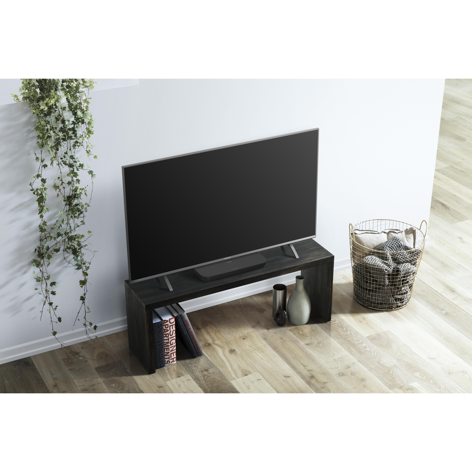 Una TV nera su un supporto in legno scuro. Un cesto e un vaso sono sul lato. Edera appesa al lato.