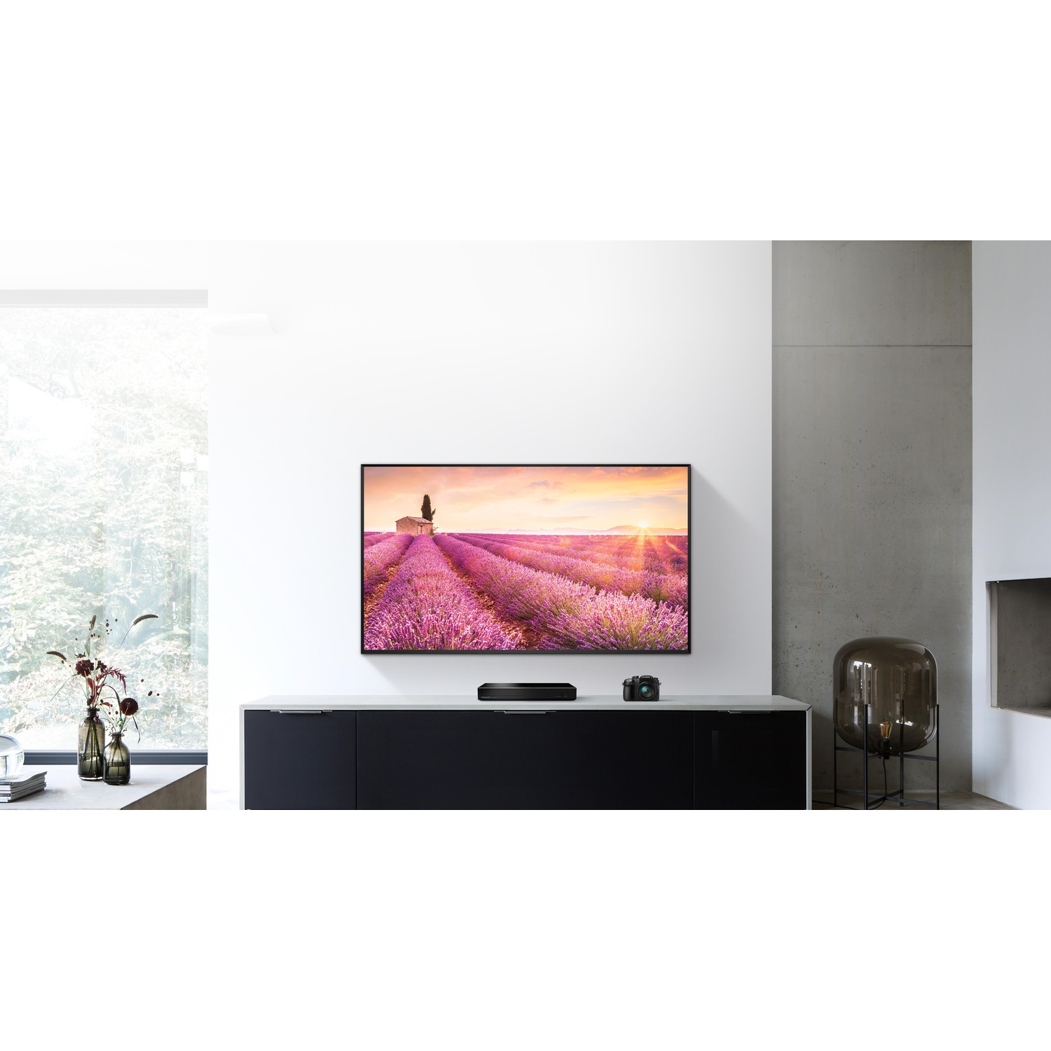 Un televisore su una console nera, che mostra una scena di campo di lavanda. Una fotocamera e delle decorazioni sono sulla console.