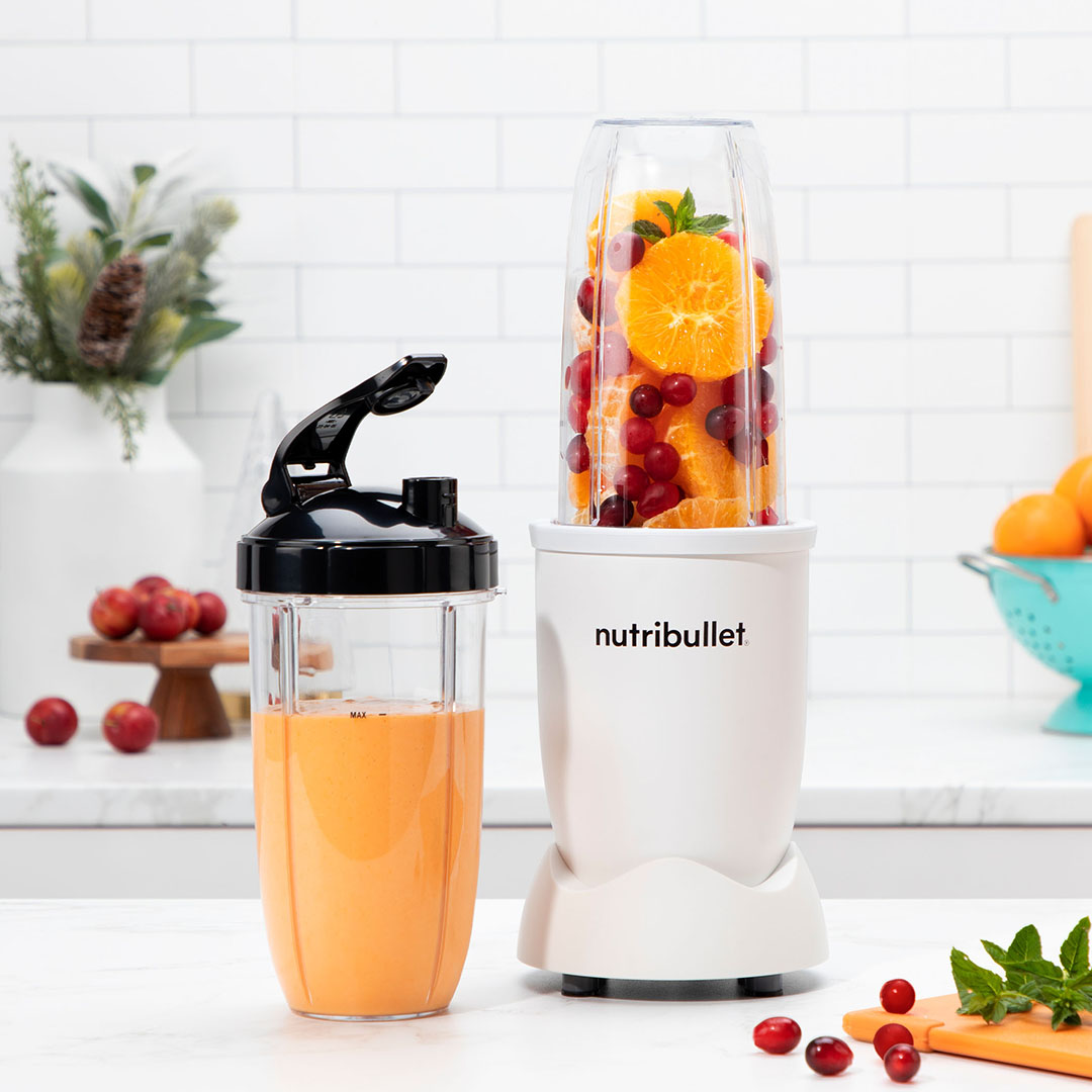 Egy Nutribullet turmixgép narancsokkal és bogyókkal. Egy másik tartály egy turmixszal mellette.