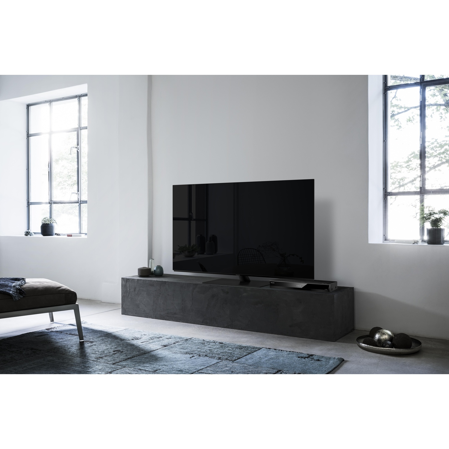 Un televisore nero è montato su un supporto grigio scuro. Sono visibili due finestre.