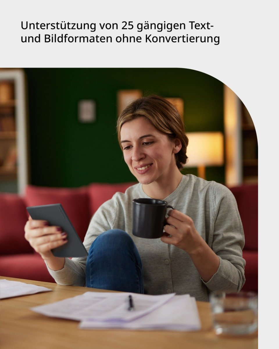 Frau sitzt an einem Holztisch, hält ein Tablet und einen Becher. Ein rotes Sofa ist im Hintergrund.