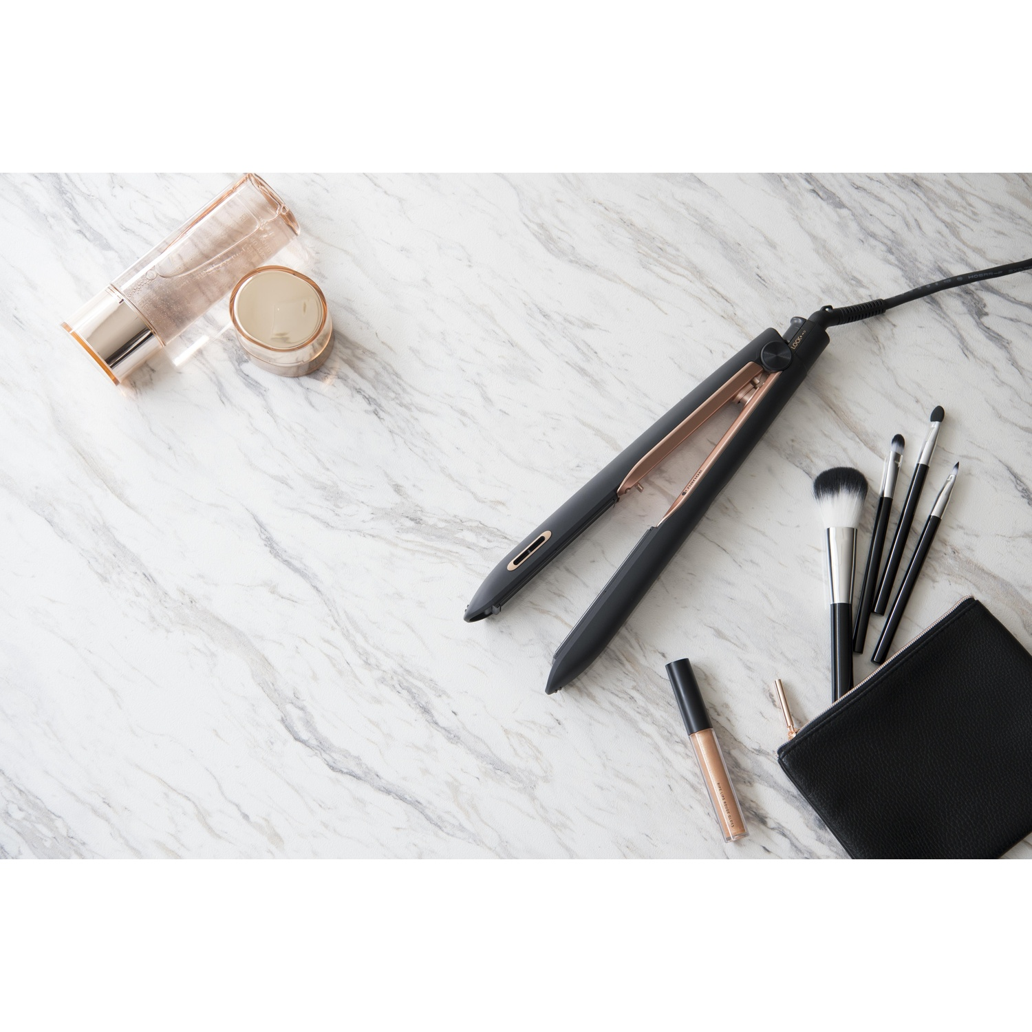 Piastra, pennelli trucco e prodotti skincare su marmo. Accenti neri e oro.