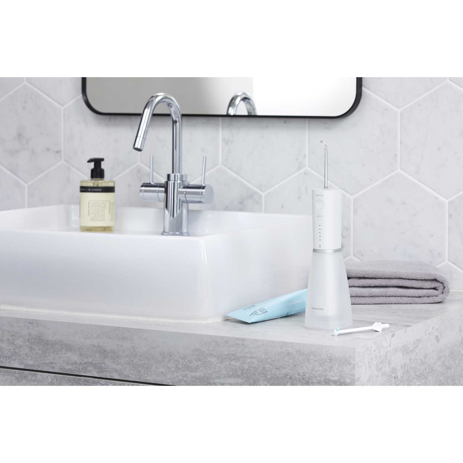 Una scena di bagno con un lavandino bianco, rubinetto e un irrigatore orale bianco.