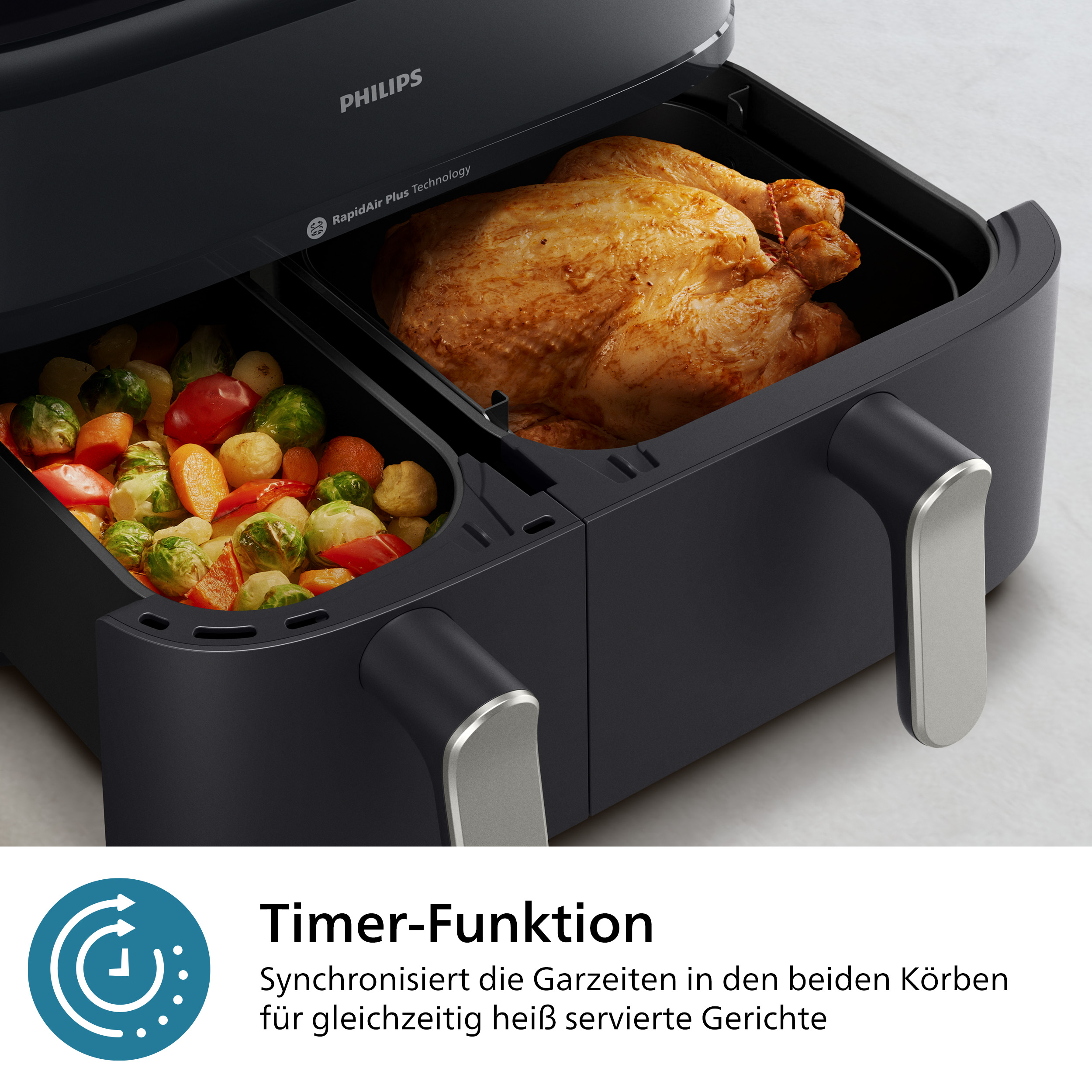 Schwarze Philips Heißluftfritteuse mit zwei Fächern, eines mit Brathähnchen, eines mit Gemüse.