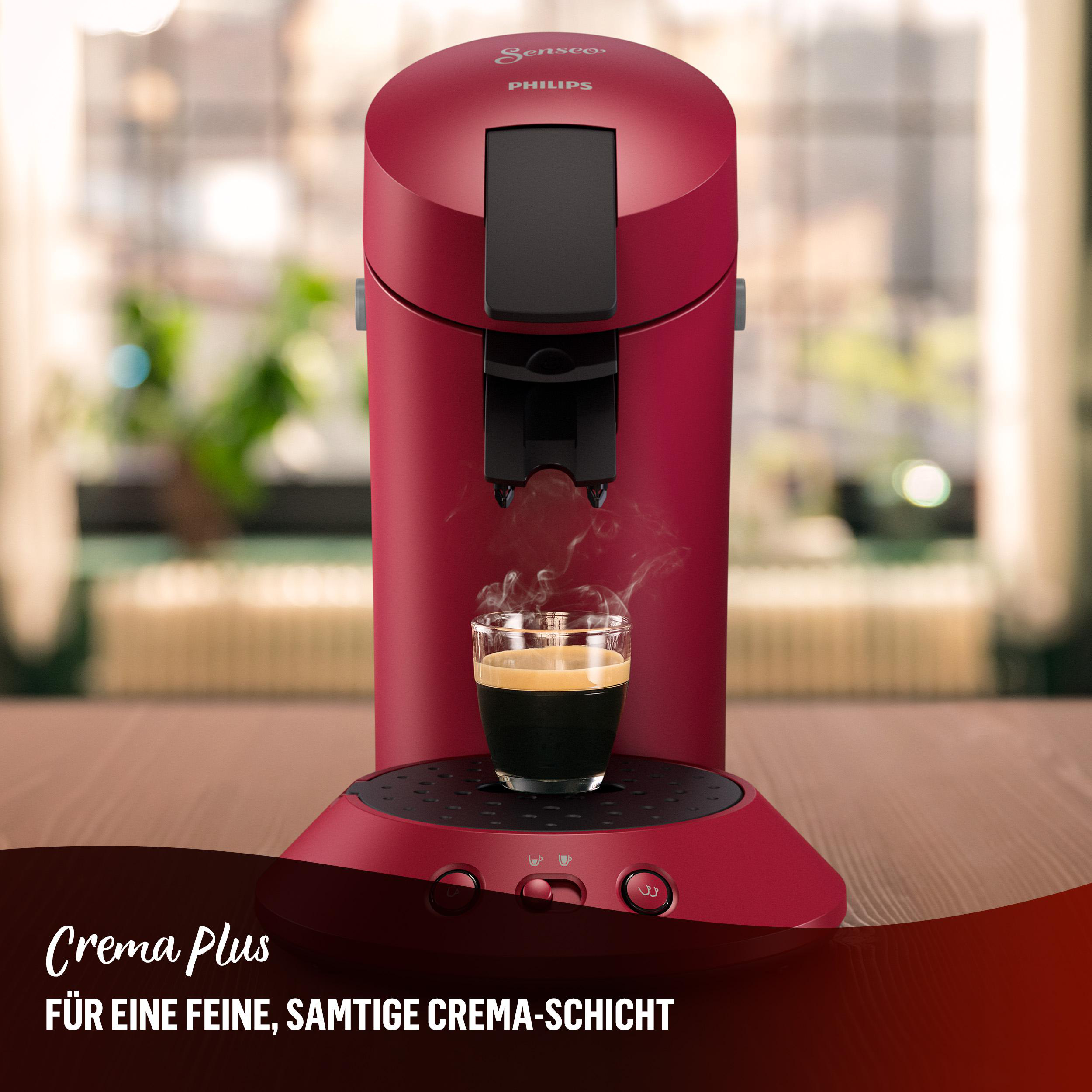 Eine rote Kaffeemaschine mit einem Glas Kaffee. Dampf steigt vom Kaffee auf.