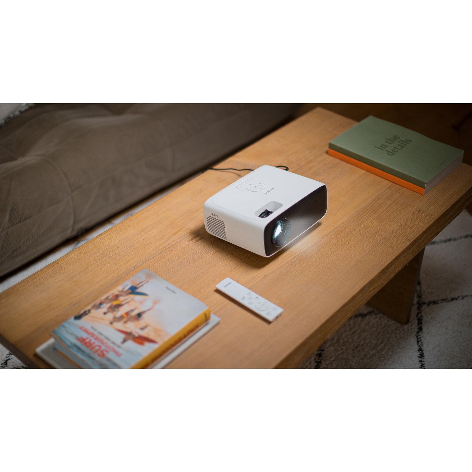 Projecteur blanc sur table en bois avec livres et télécommande. Canapé en arrière-plan.