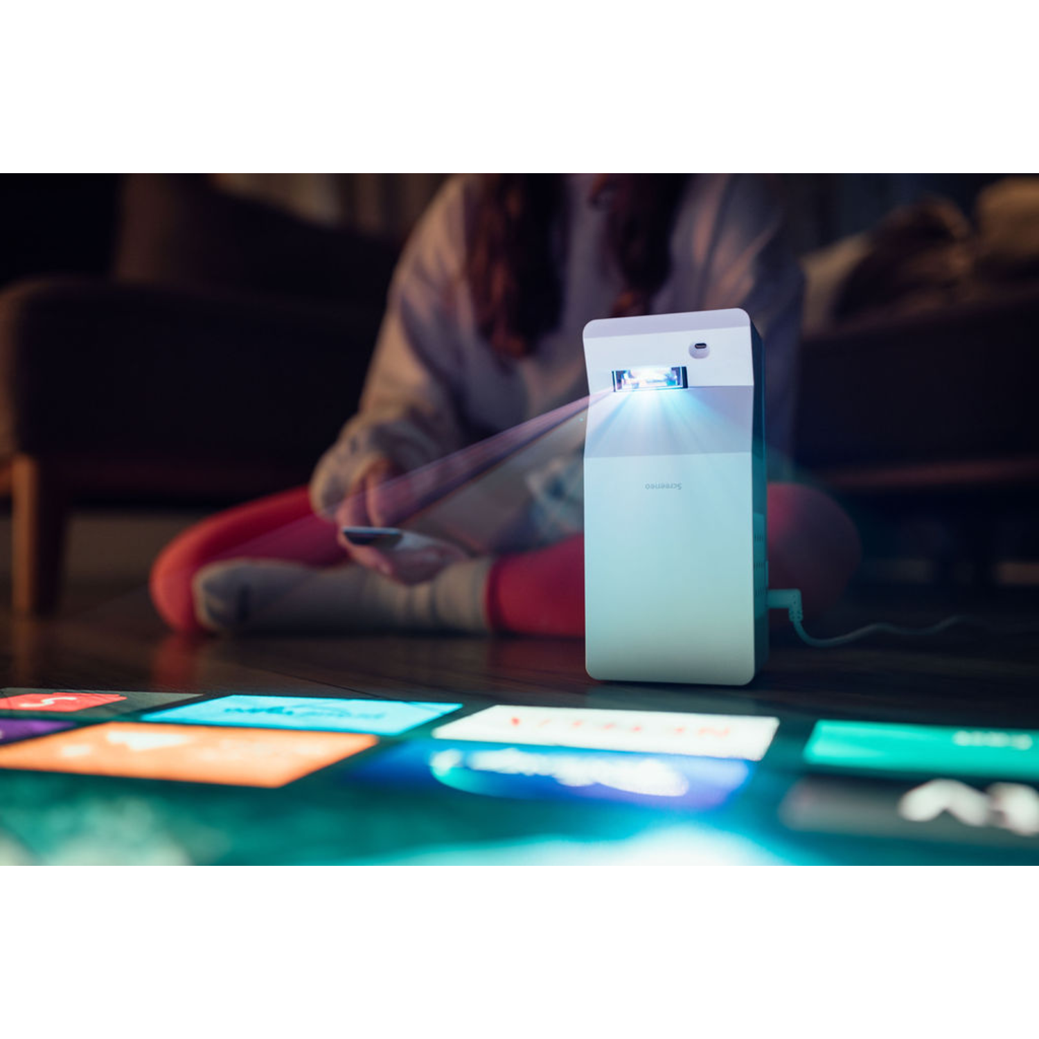 Un petit projecteur projetant sur une surface avec plusieurs images colorées, utilisé par une personne.