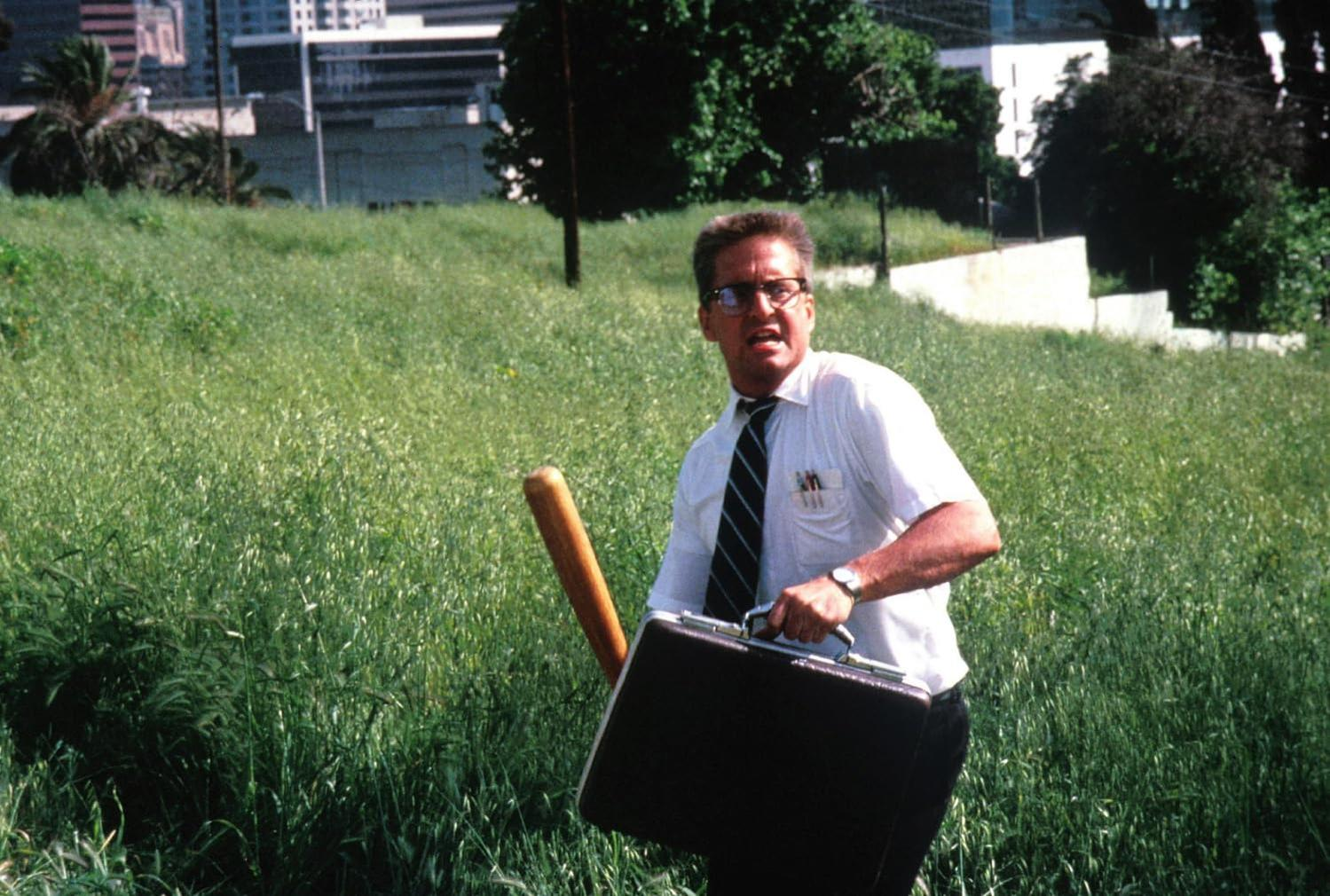 Ein Mann in einem weißen Hemd und Krawatte mit Aktenkoffer und Baseballschläger im Gras.