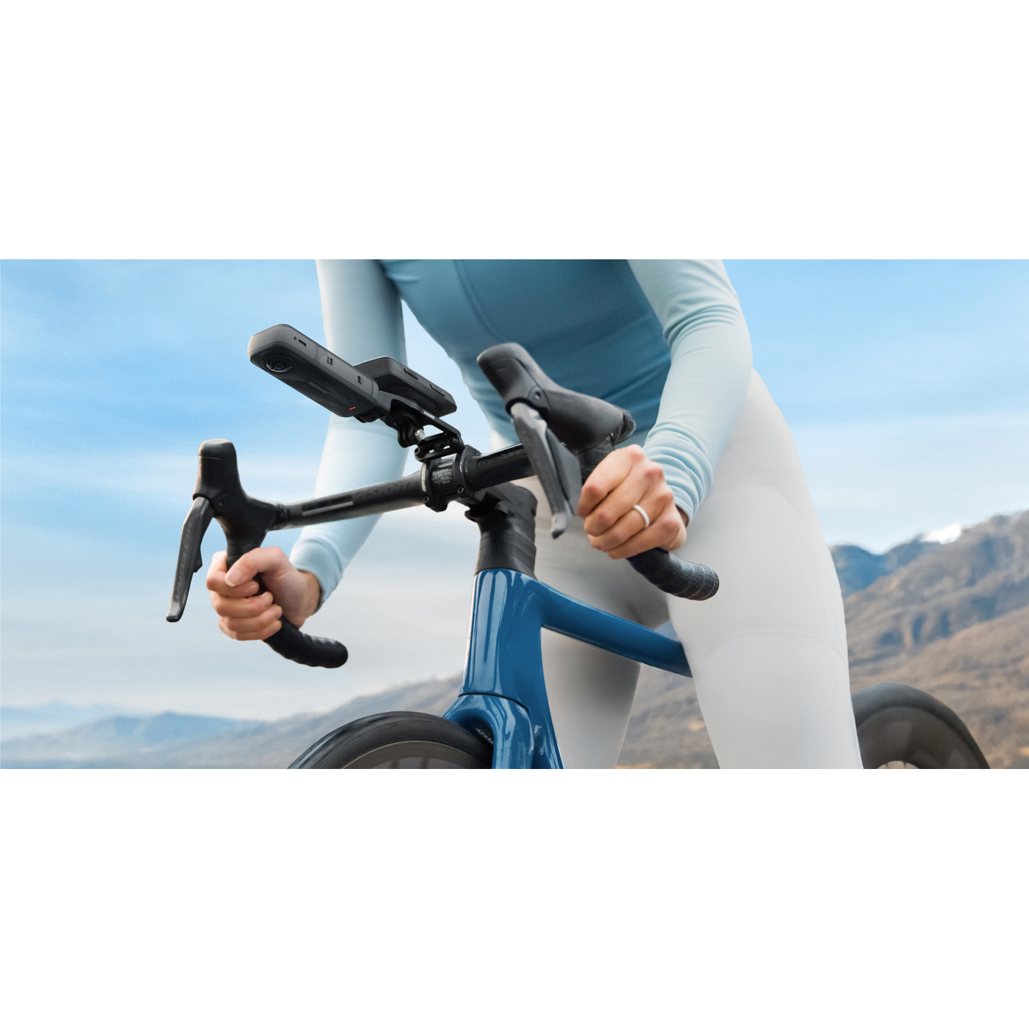 Cyclist on blue bike, hands on handlebars, mountains in background.