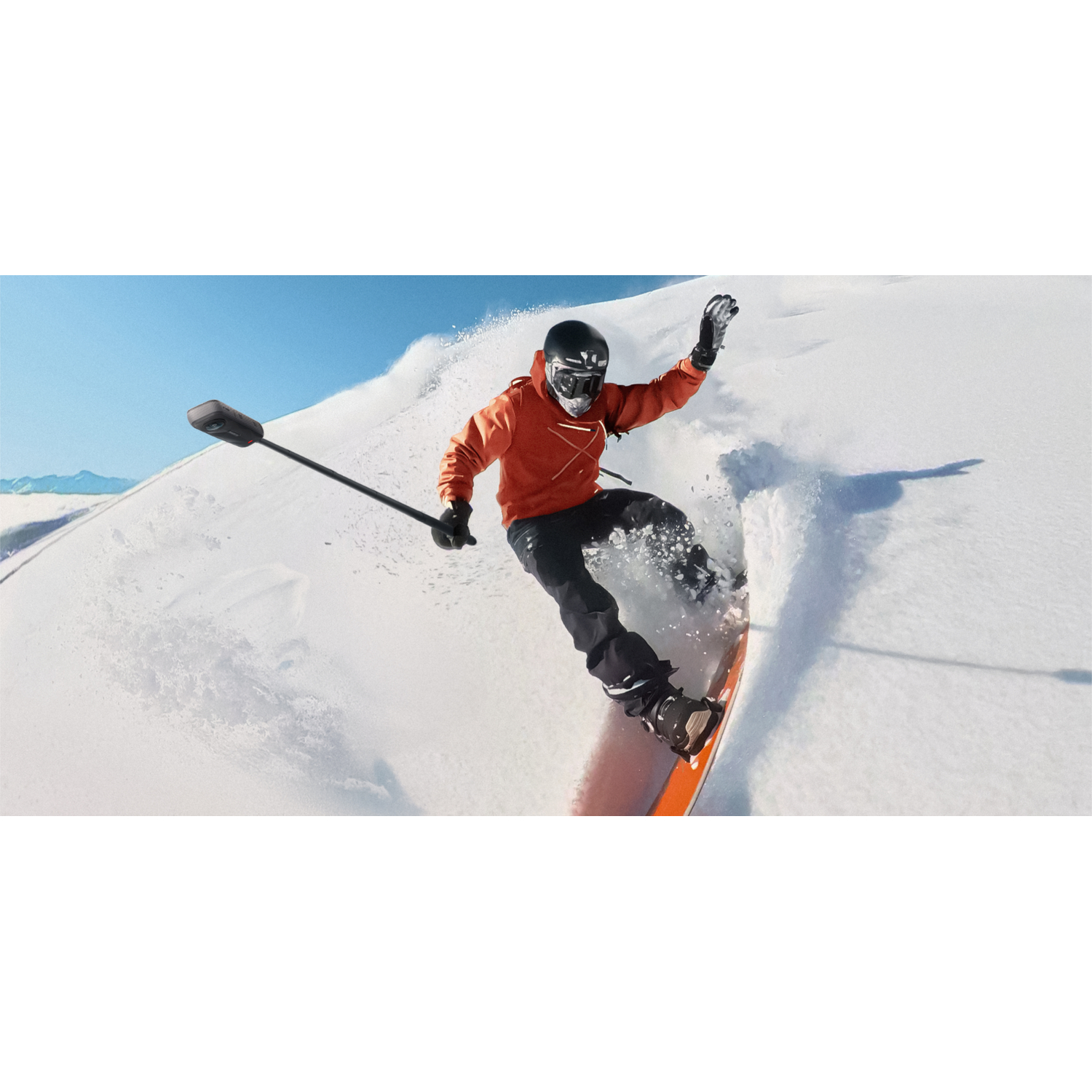 A snowboarder on a snowy mountain, filming with a stick camera.