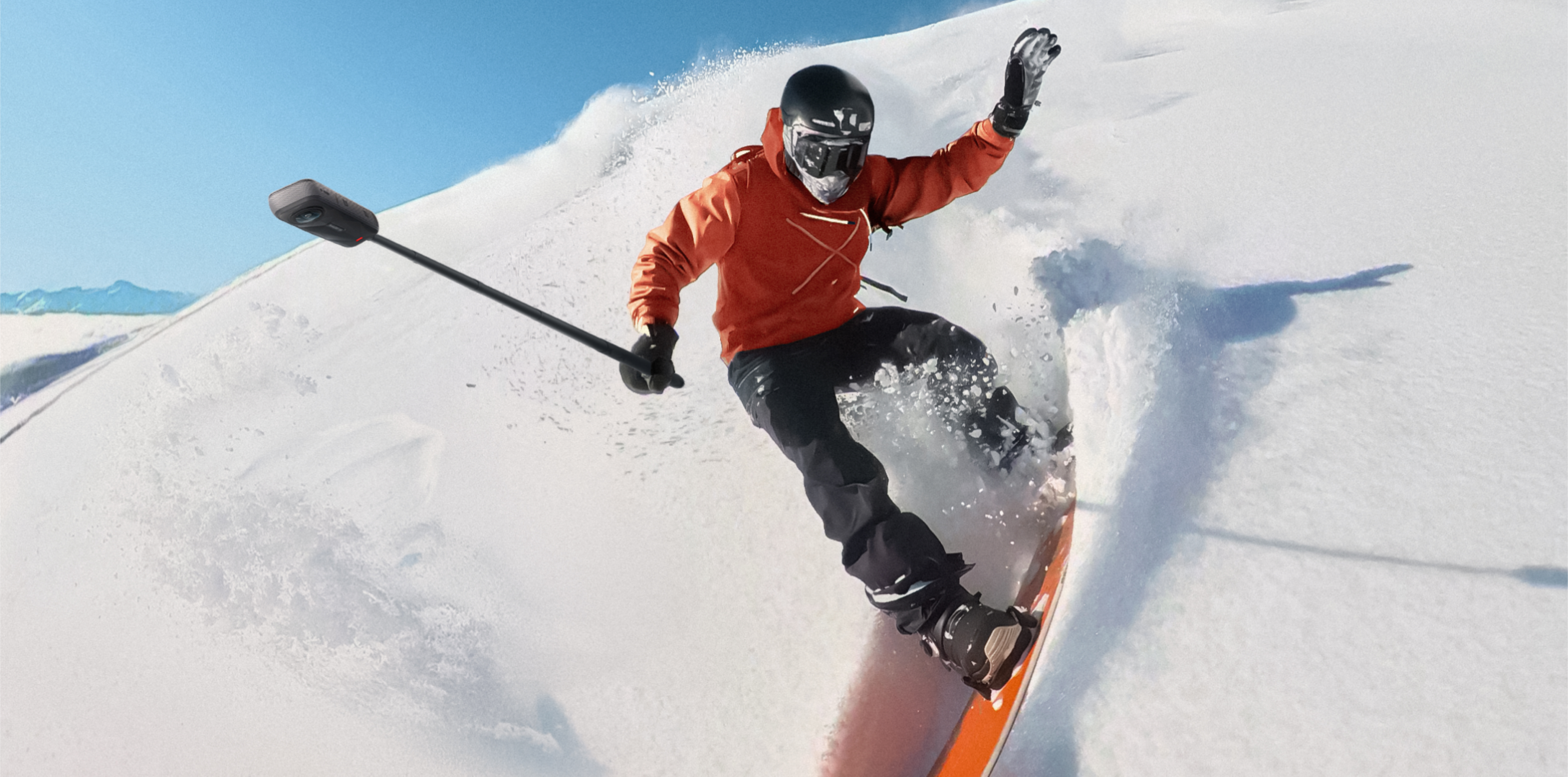 Snowboarder en veste orange dévalant une pente enneigée par une journée ensoleillée.