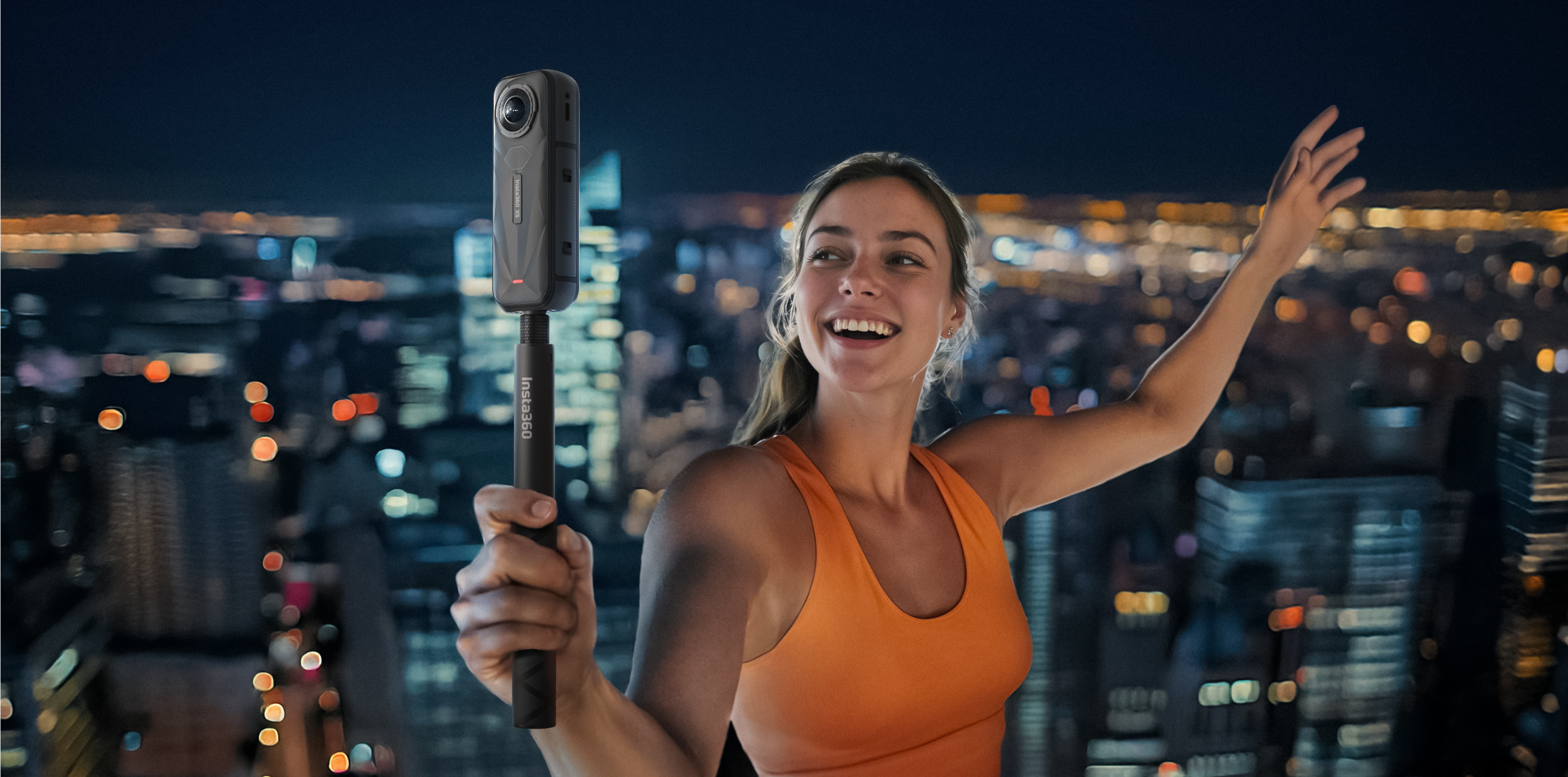 Une femme tenant un bâton à selfie avec une caméra au-dessus, debout sur un toit la nuit.