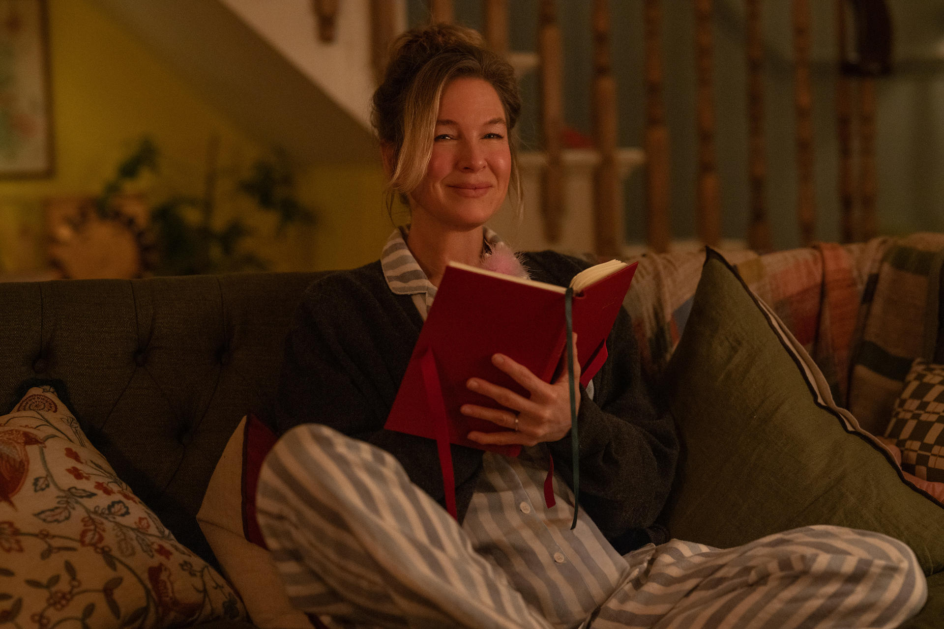 Eine Frau in Pyjamas liest ein rotes Buch auf einem Sofa.