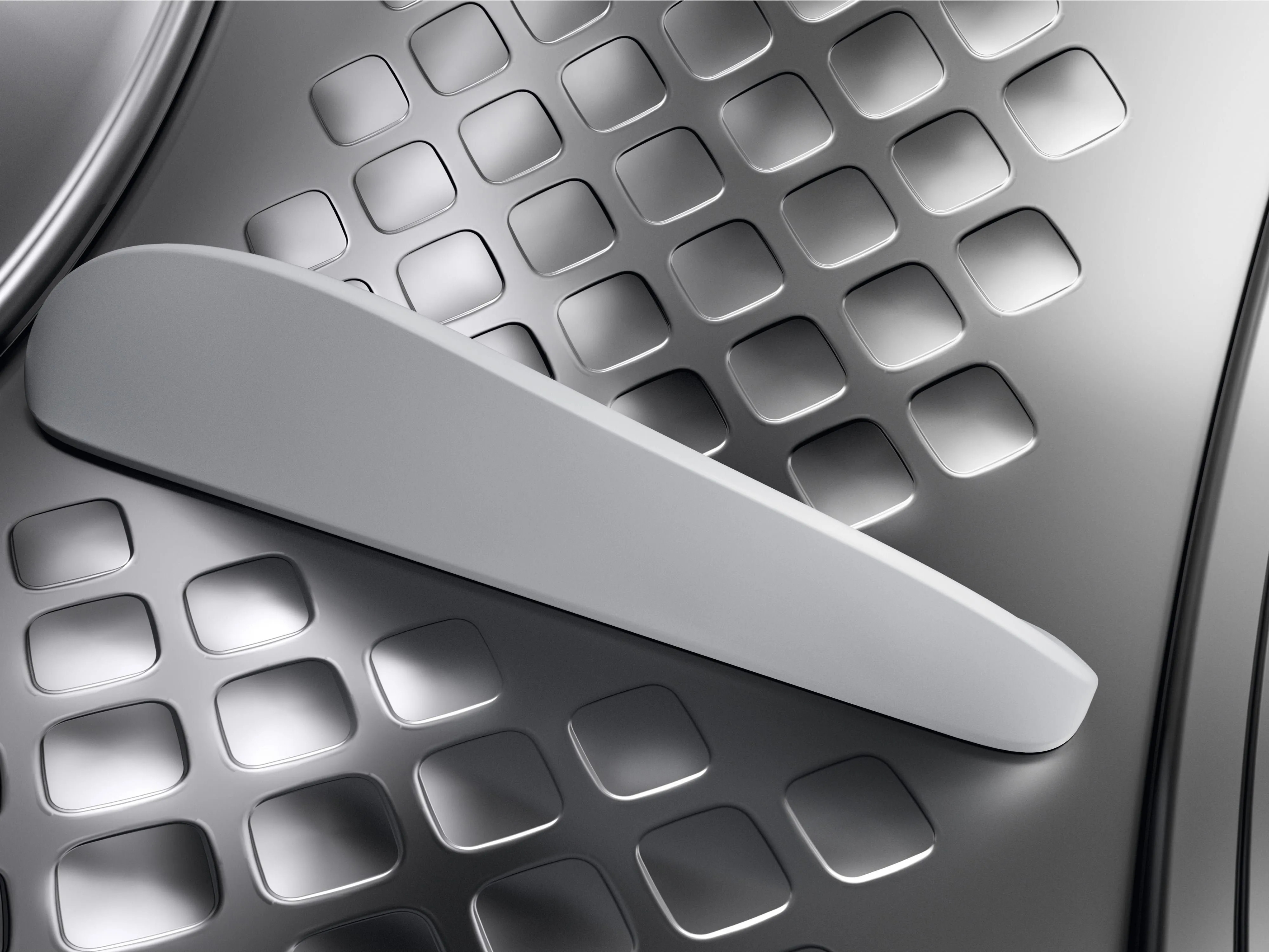 Zbliżenie na metalowy element pralki z białym uchwytem.